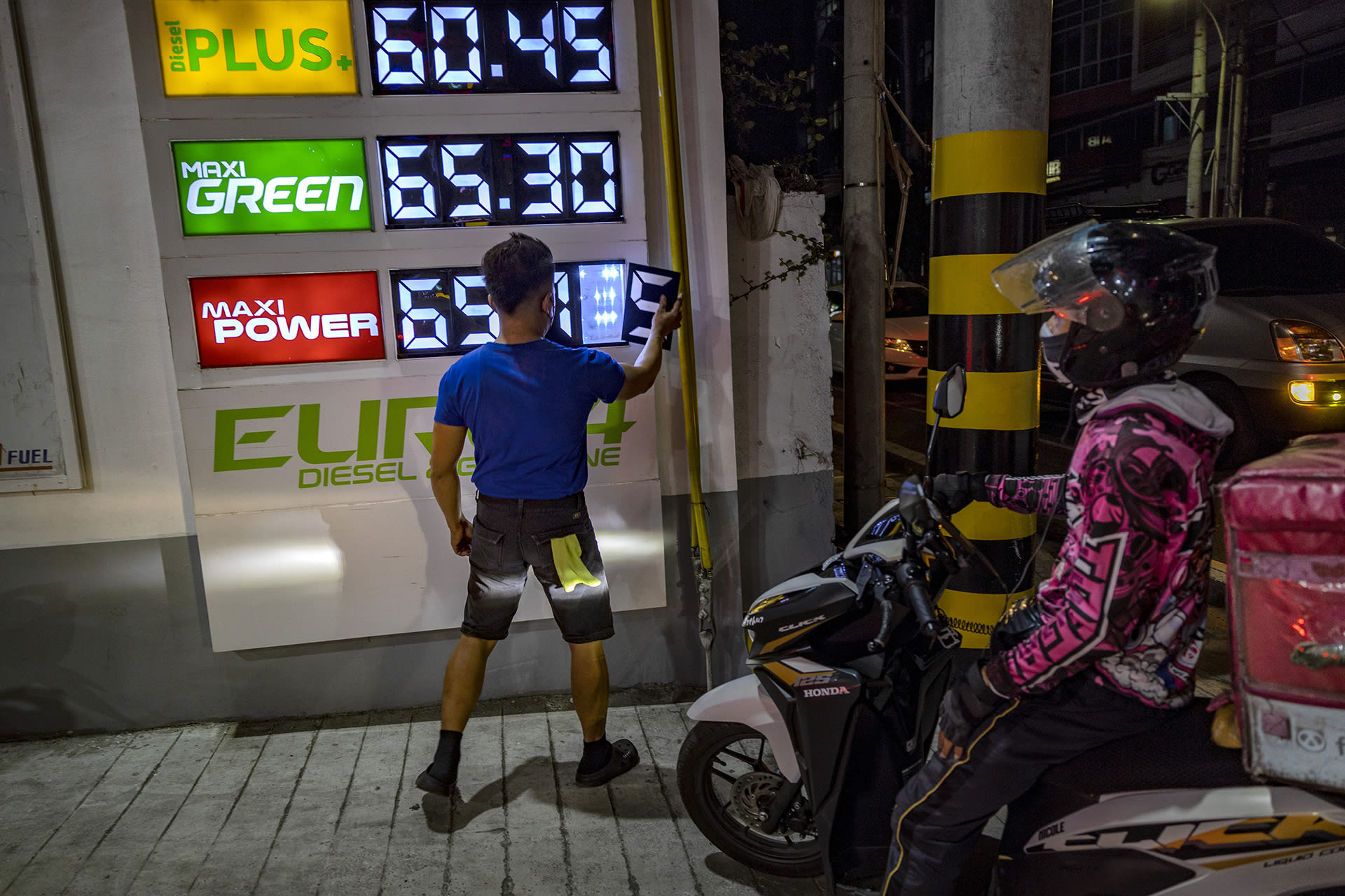 A man faces a gas price billboard and changes the numbers of the price displayed.