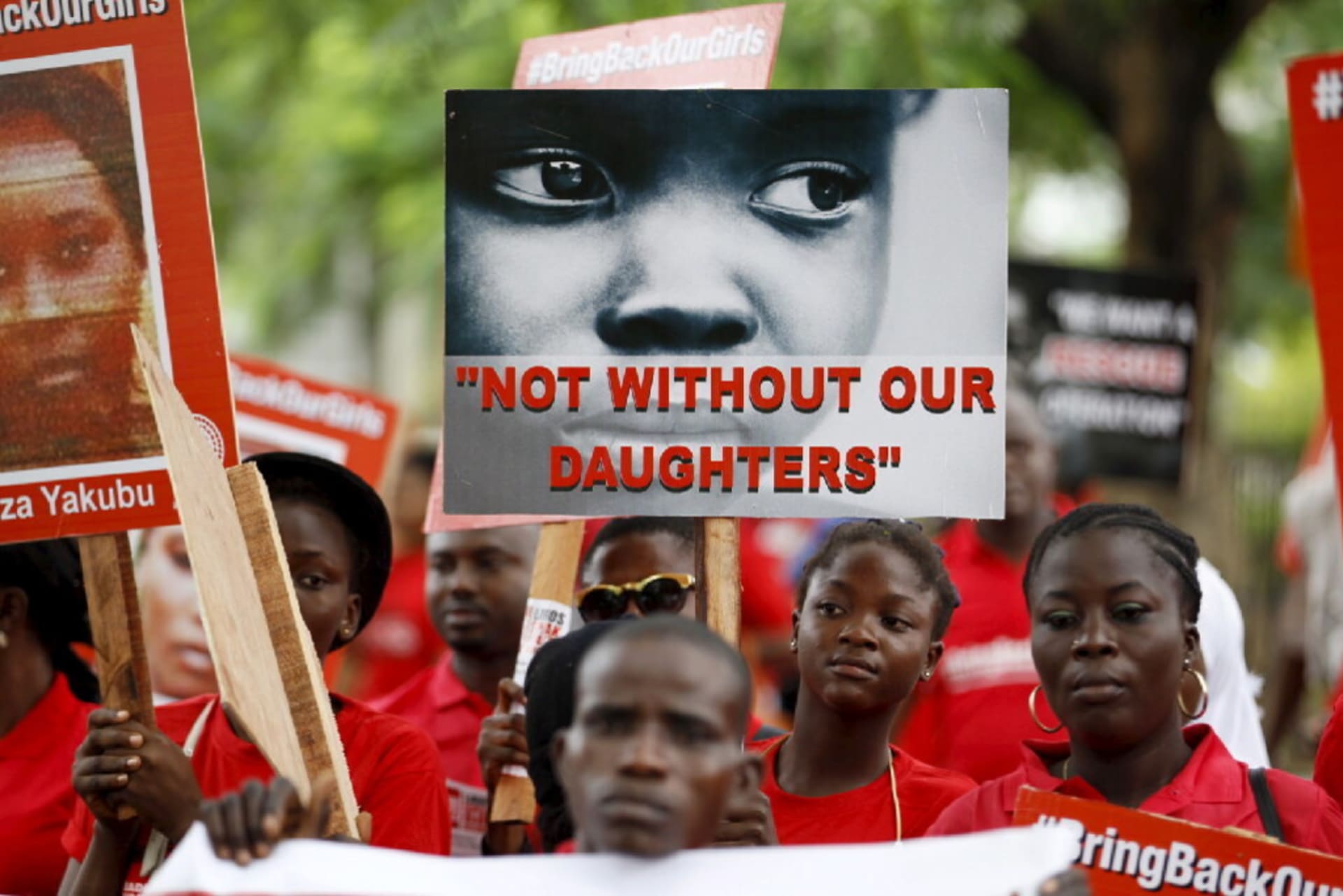 A girl holding a sign at a protest that says "NOT WITHOUT OUR DAUGHTERS".