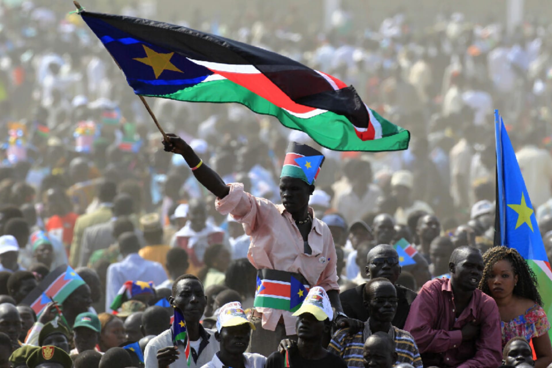 A person waving the South Sudanese flag in a crowd full of people.
