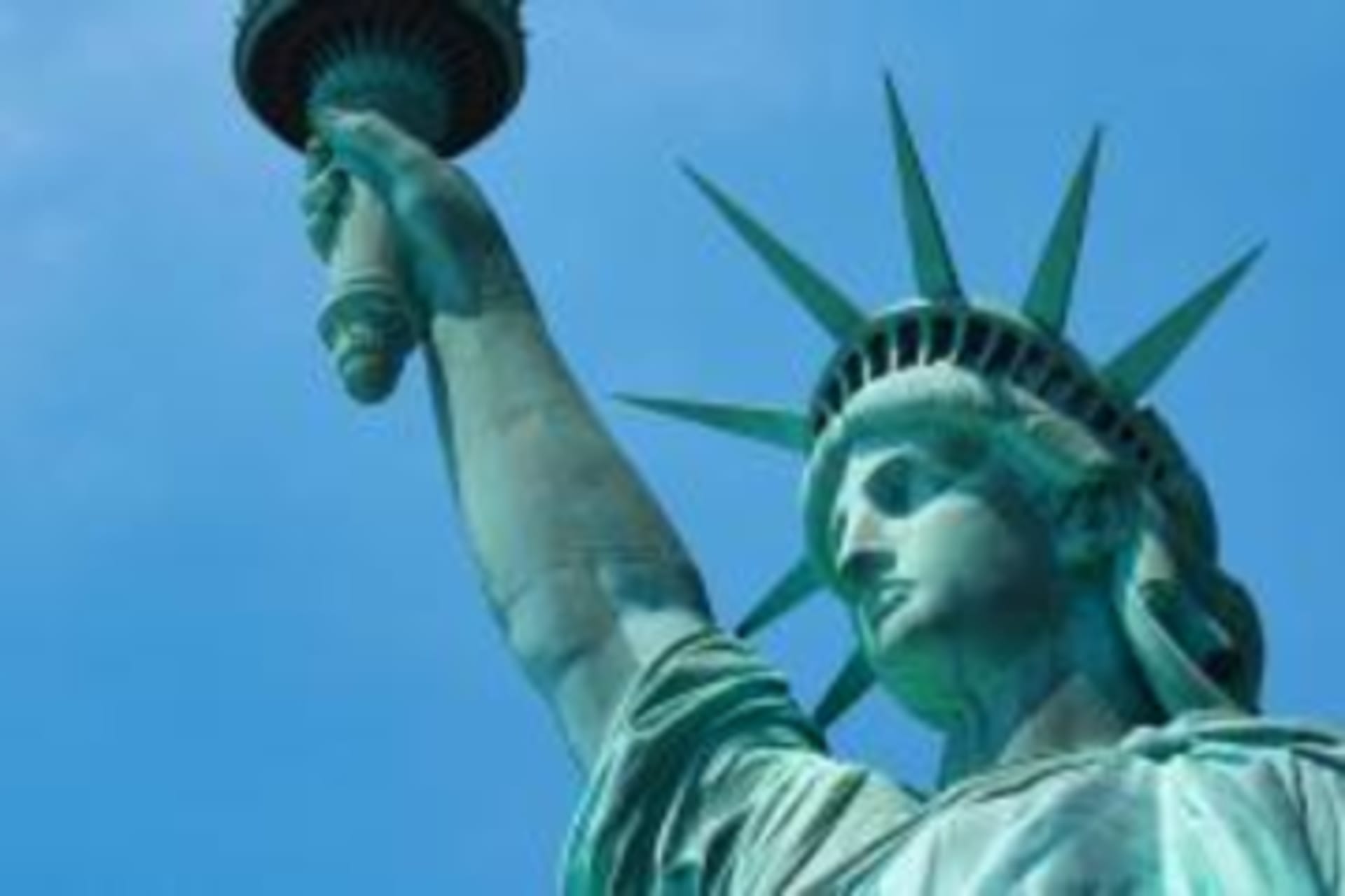 A close up shot of the Statue of Liberty underneath a blue sky.