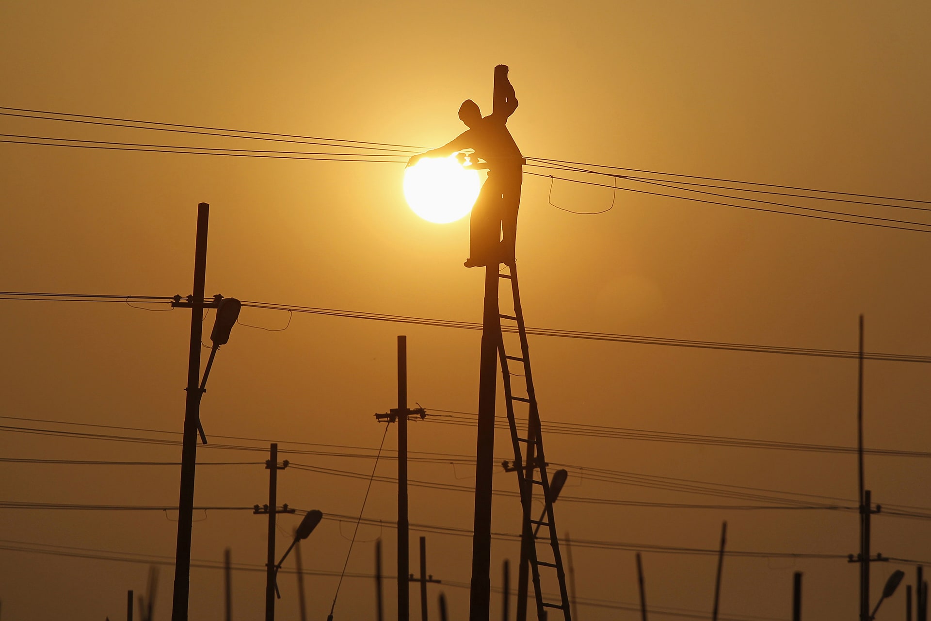 A worker is silhouetted against the setting sun while installing an overhead electric cable pole on the banks of river Ganges in Allahabad