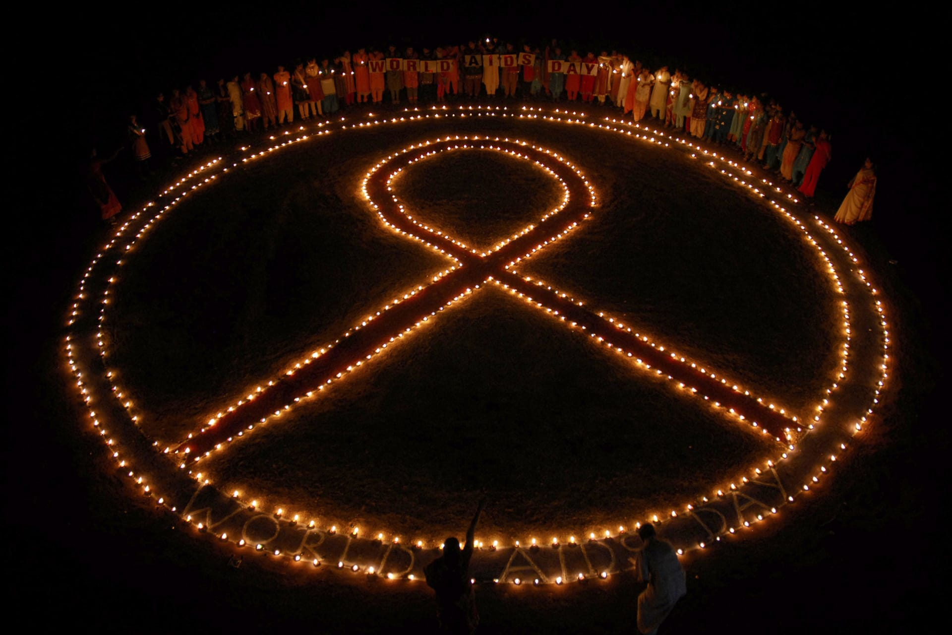 Students hold oil lamps beside a symbol of AIDS in Chennai