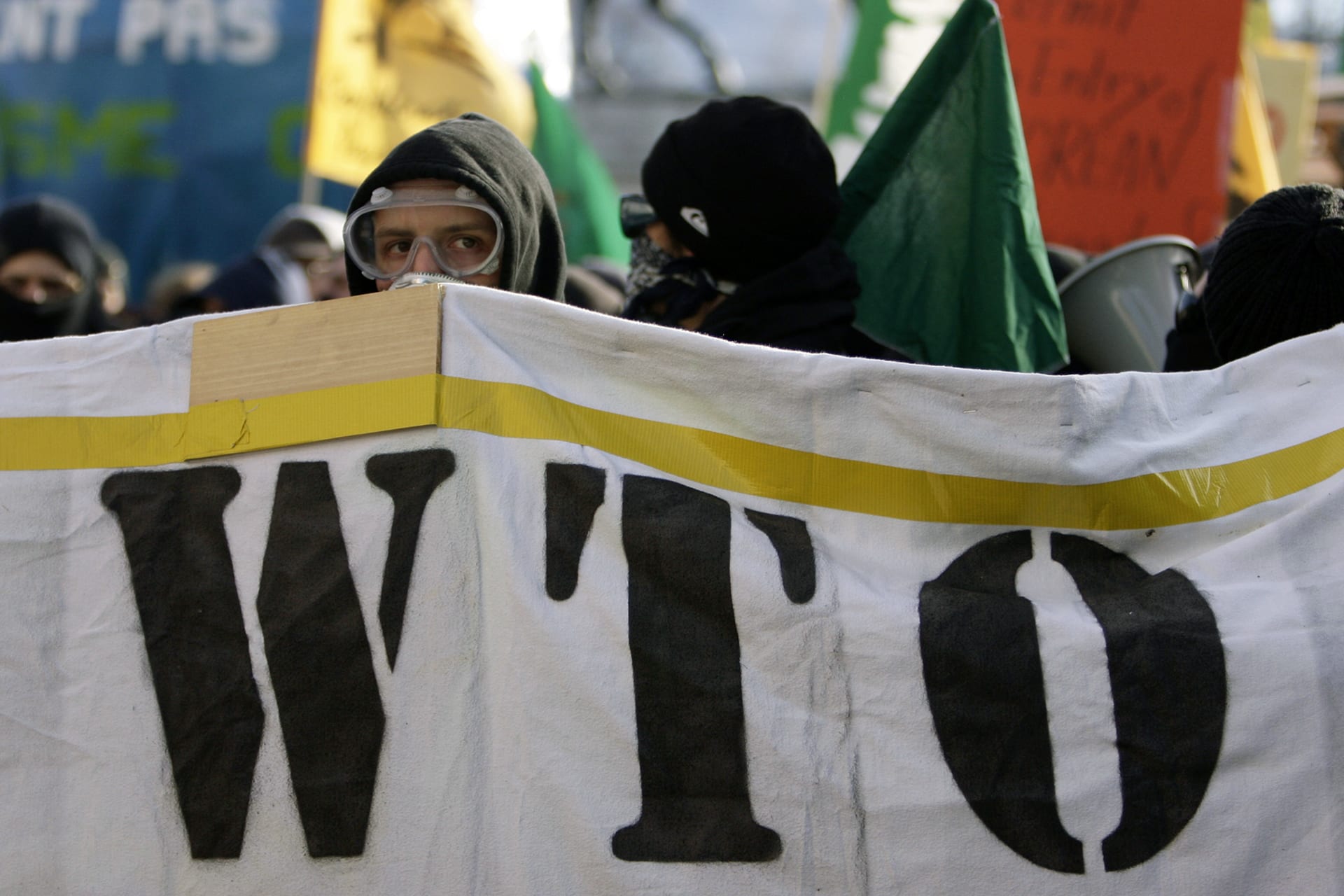 An anti-capitalism demonstrator looks behind a WTO poster during a protest against the World Trade Organisation in Geneva