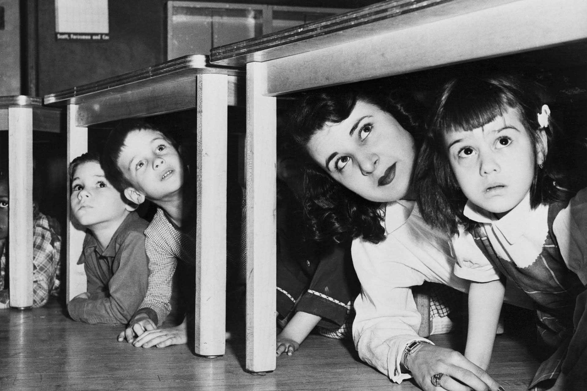 Teacher And Children Crouching Under Table