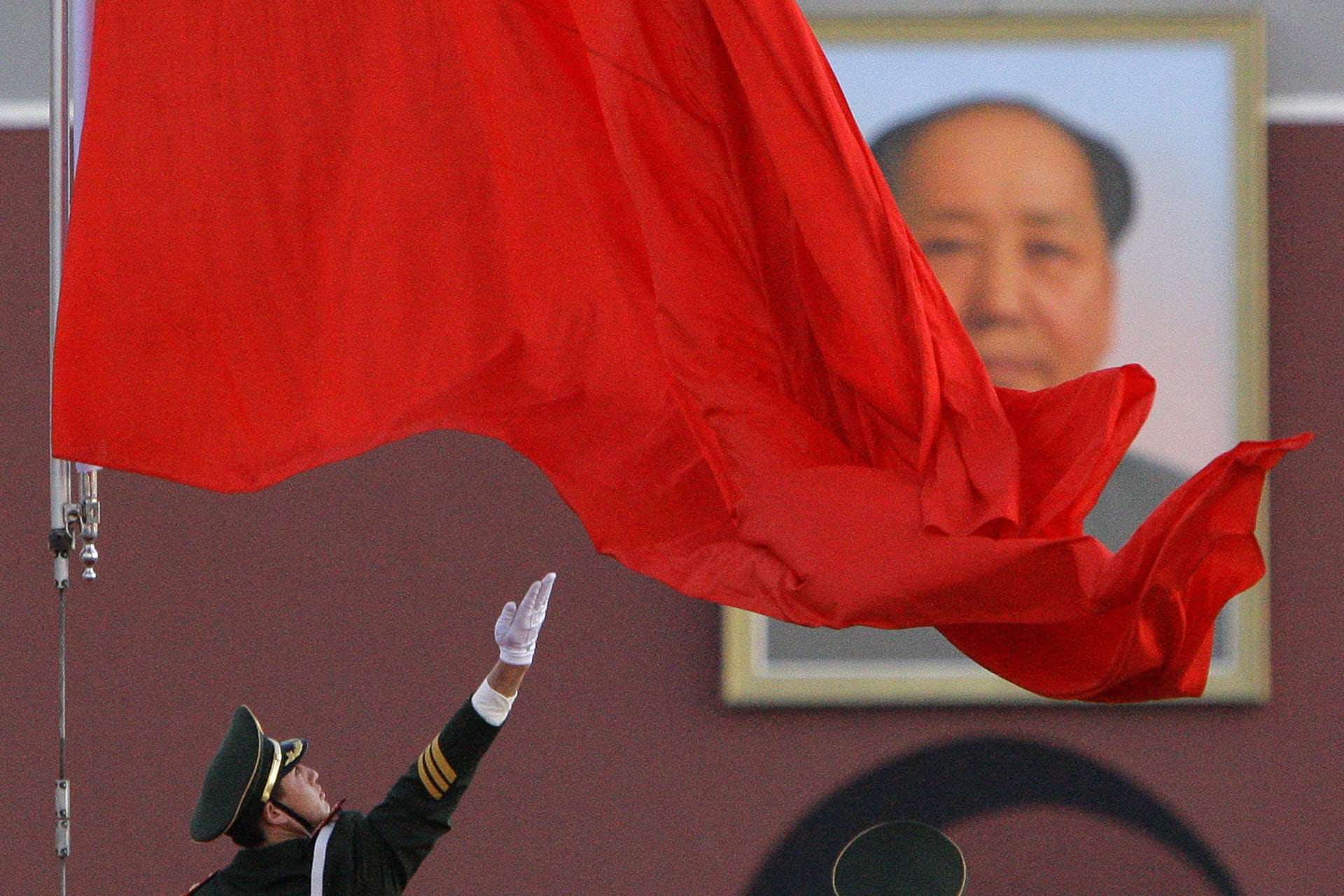 A soldier unfurls the Chinese national flag as it is raised in front of the giant portrait of Chairman Mao Zedong in Beijing's Tiananmen Square