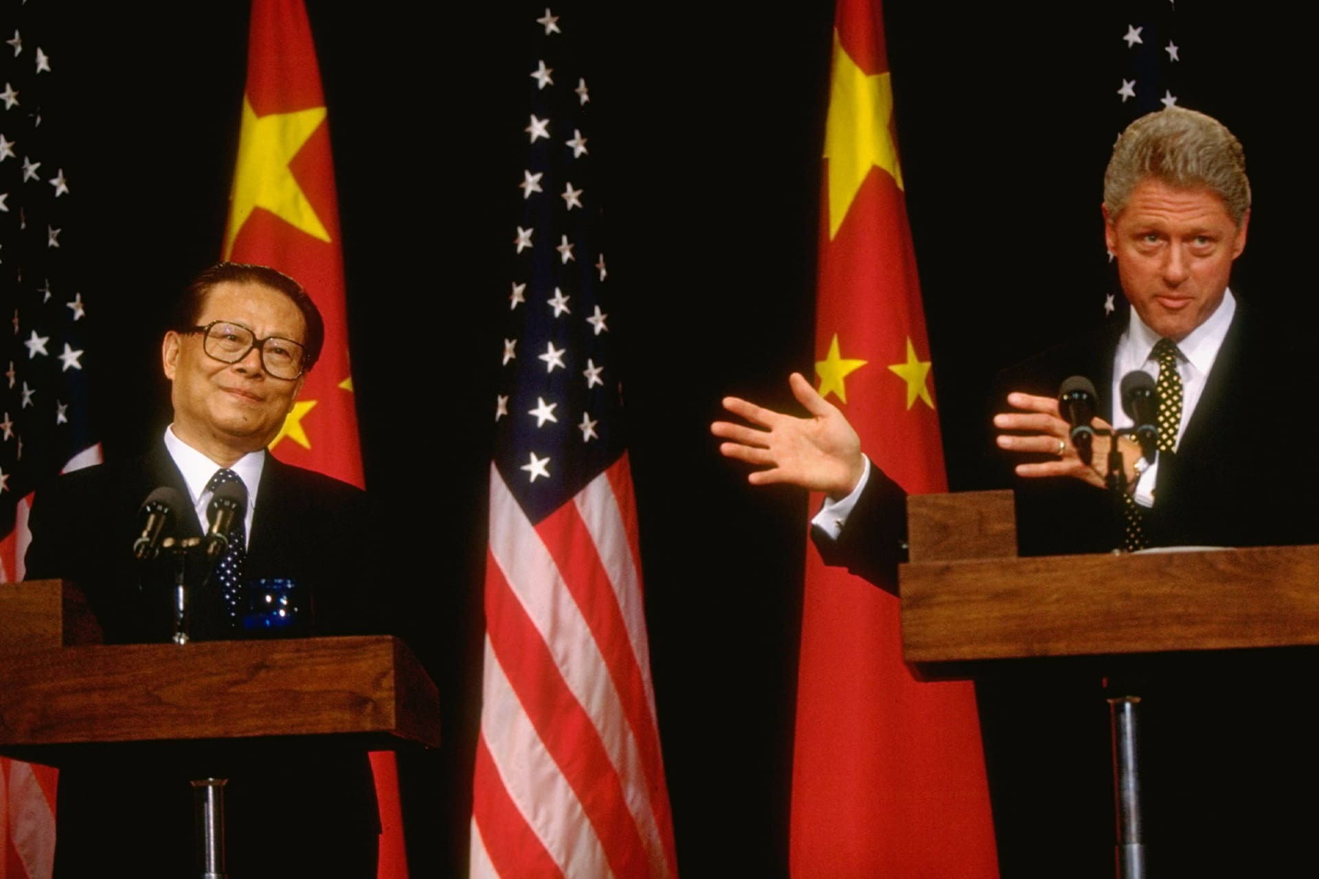 President Bill Clinton points to Chinese leader Jiang Zemin during joint press conference in front of U.S. and Chinese flags.