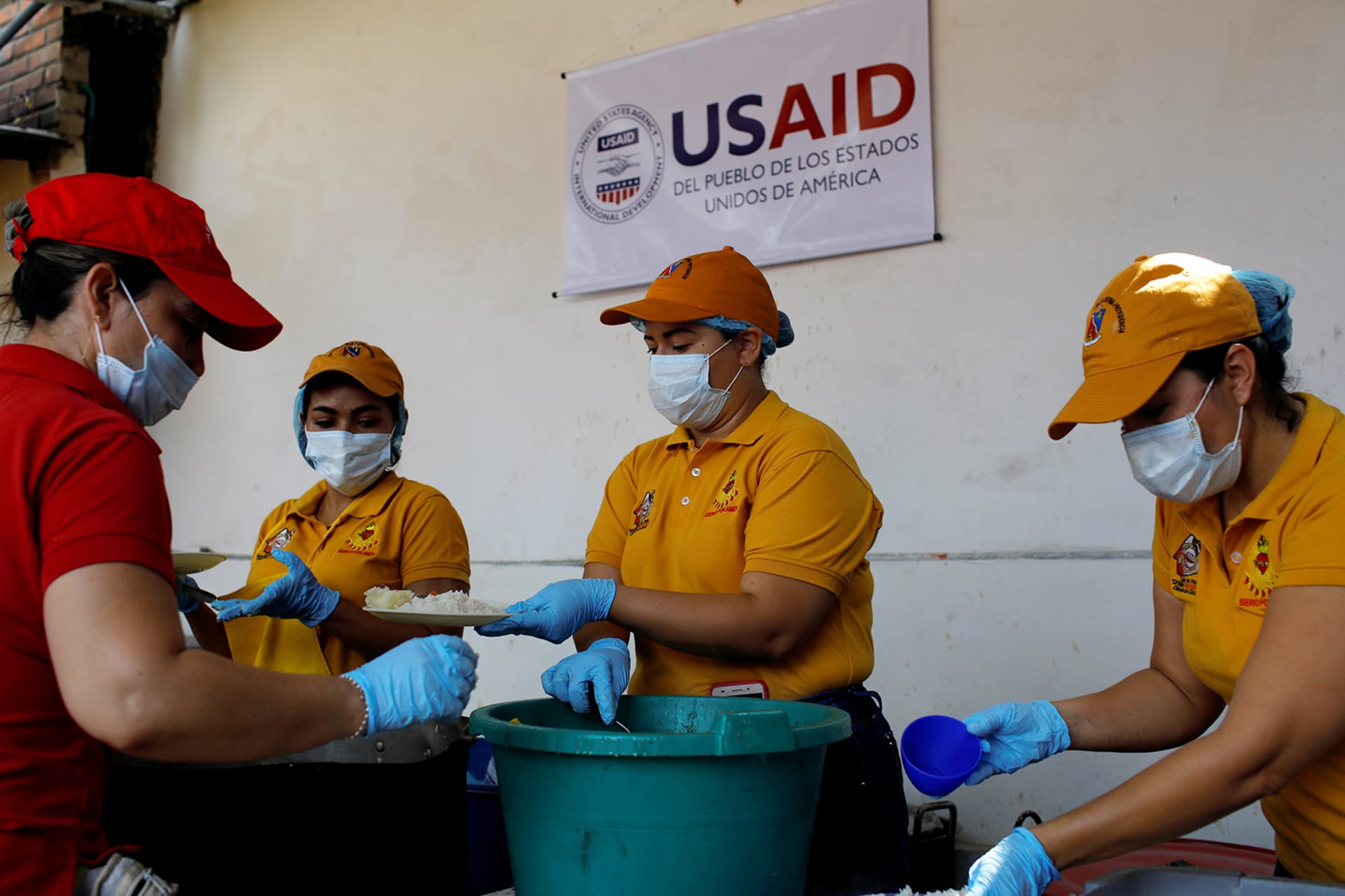 Volunteers serve lunch in a community kitchen set up by USAID and World Food Programme in Cucuta, Colombia. There is a sign behind them that reads, "USAID Del Pueblo de Los Estados Unidos de America".