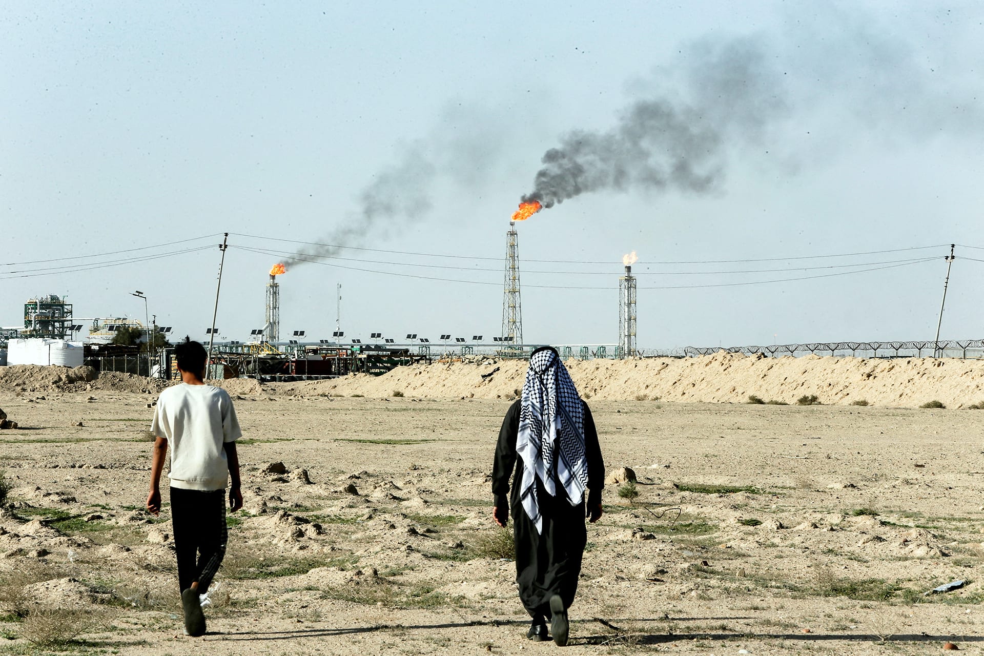 People walk near farmland by the Zubair oil field as gas flares rise in the distance, in Zubair Mishrif, Basra, Iraq, amid regional tensions following the recent disruption to shipping in the Strait of Hormuz and the U.S.-Israeli conflict with Iran on March 9, 2026.