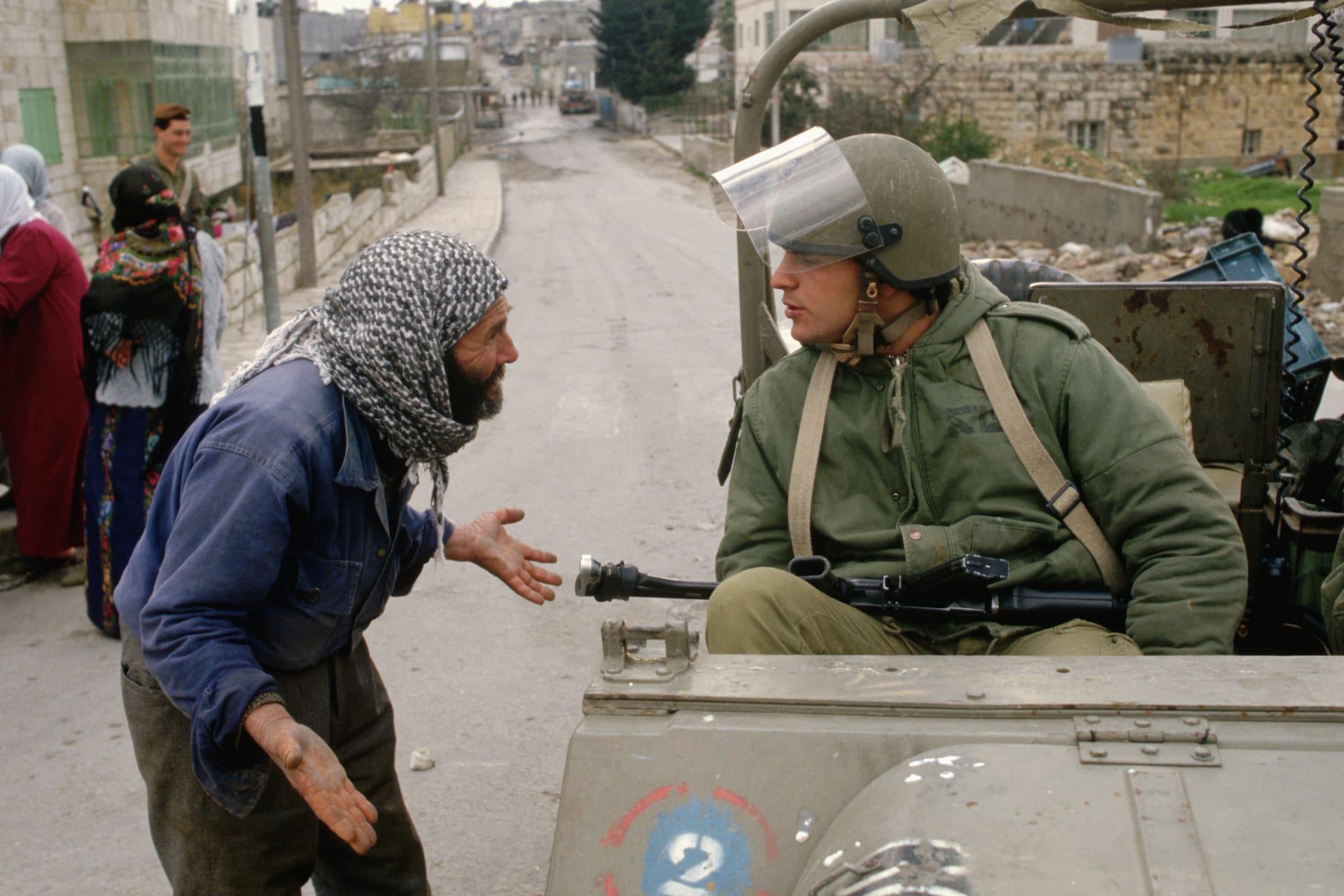 Palestinian man pleads with an Israeli soldier sitting in a military vehicle.