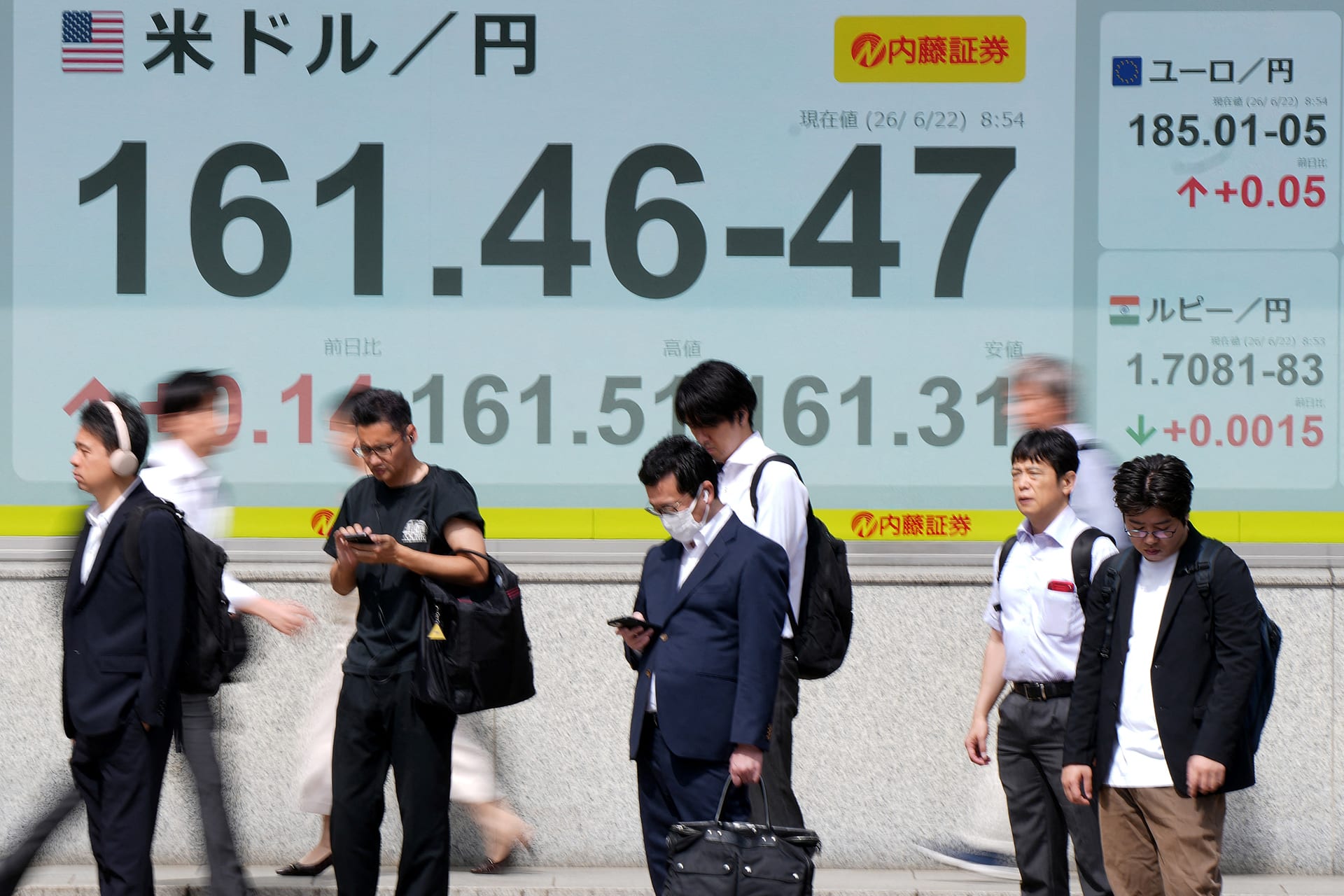 Pedestrians stand in front of electronic boards displaying the foreign exchange rate of the Japanese yen against the US dollar (L) and other currencies (R), along a street in Tokyo on June 22, 2026.