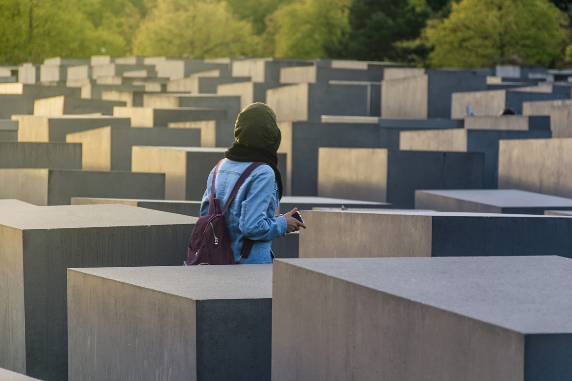 Woman with a red backpack walks through Holocaust memorial in Berlin.