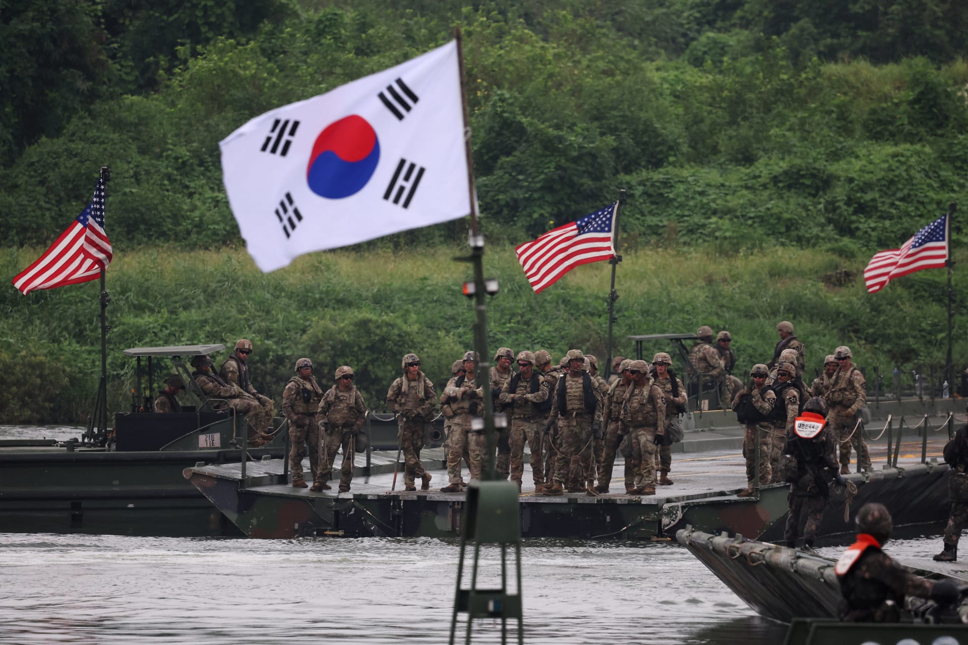 A South Korean flag flutters in the foreground as U.S. and South Korean army soldiers take part in a joint river-crossing exercise.