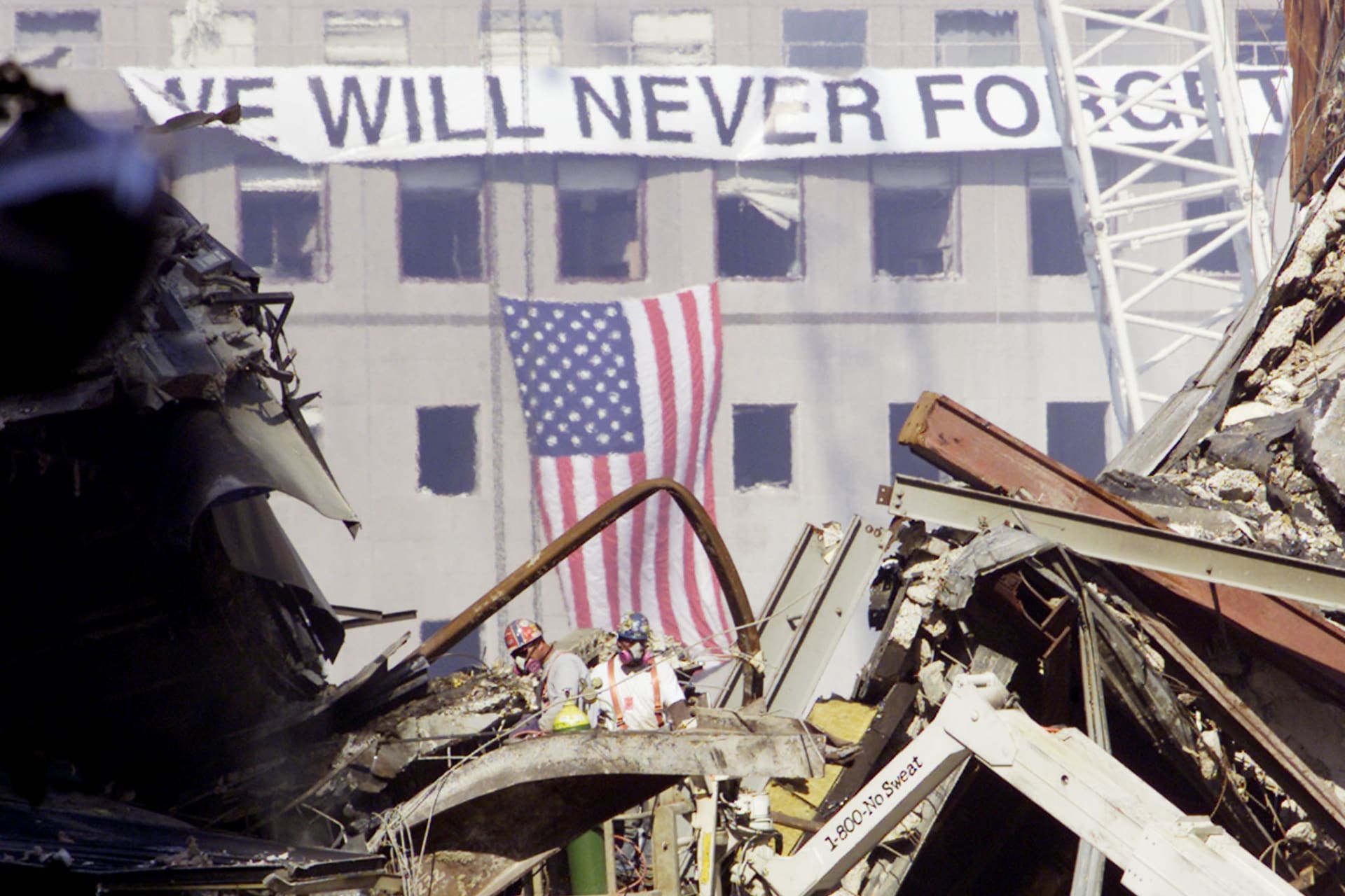Workmen cut through steel as they continue to work on the smoldering remains of the collapsed World Trade Center buildings in New York, on September 23, 2001. There is a banner that reads "We Will Never Forget" and and American flag hanging from it in the background.