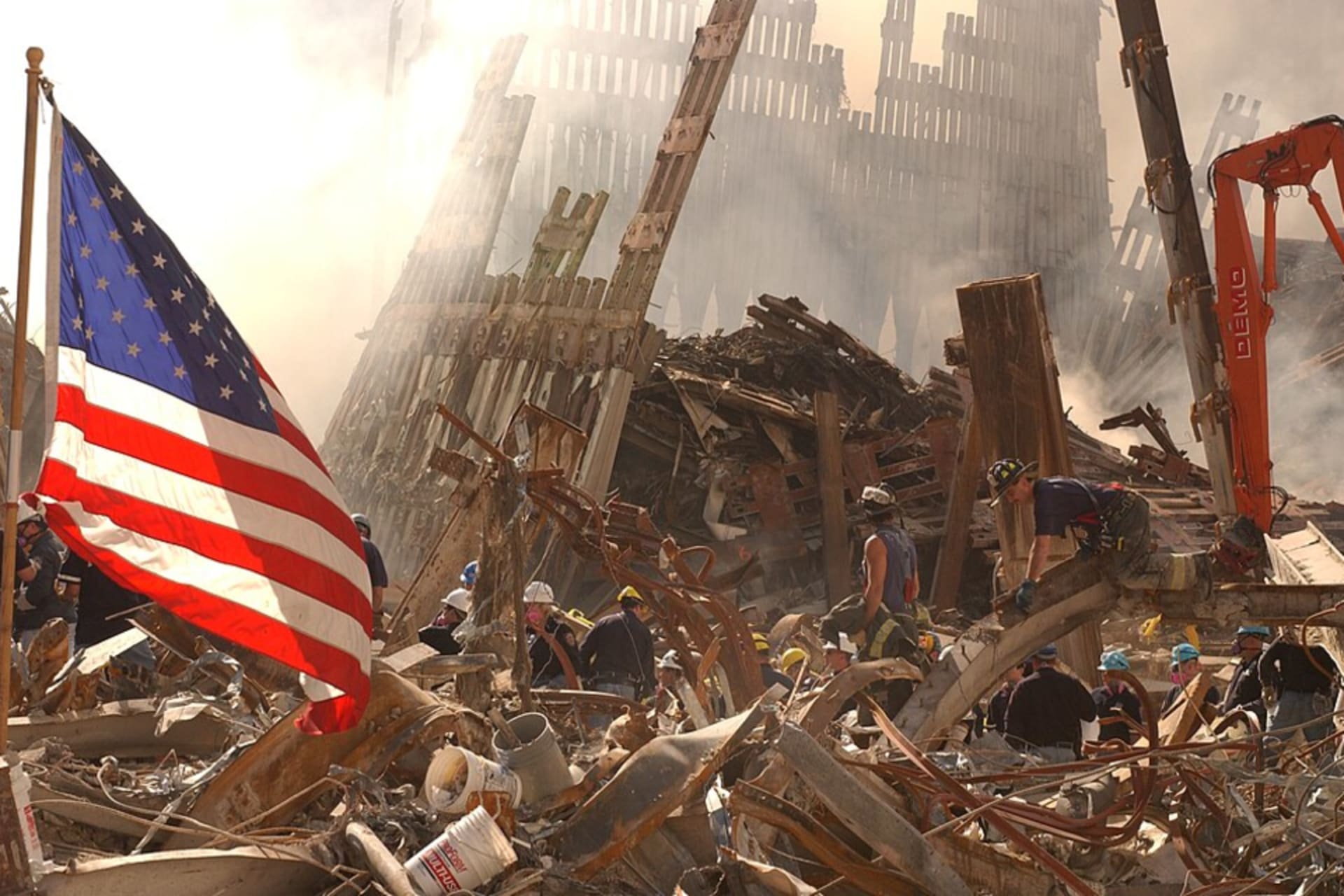<p>Rescue workers climb over and dig through piles of rubble from the destroyed World Trade Center as the American flag billows over the debris.</p>
