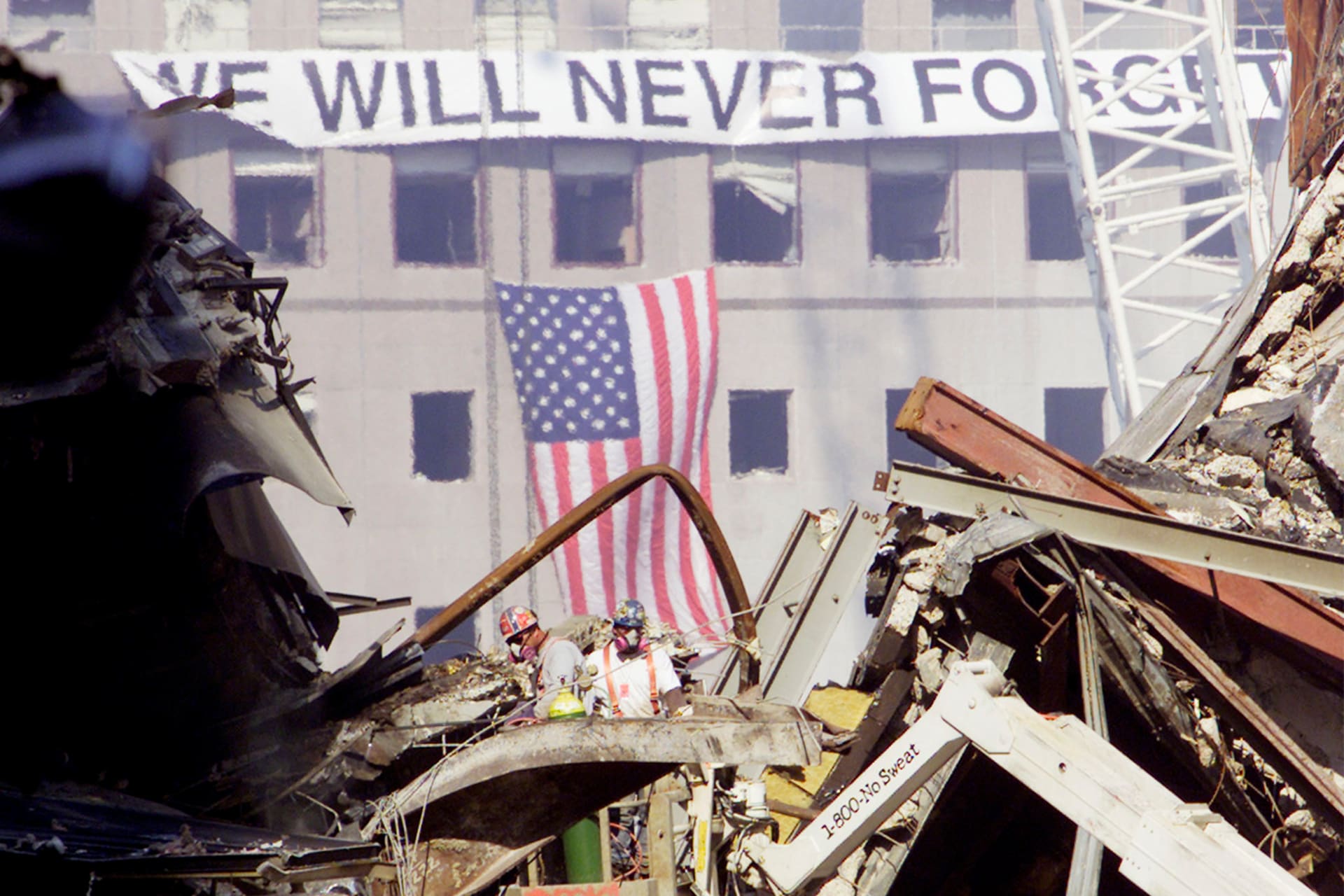 Workmen cut through steel as they continue to work on the smoldering remains of the collapsed World Trade Center buildings in New York, on September 23, 2001. There is a banner that reads "We Will Never Forget" and and American flag hanging from it in the background.