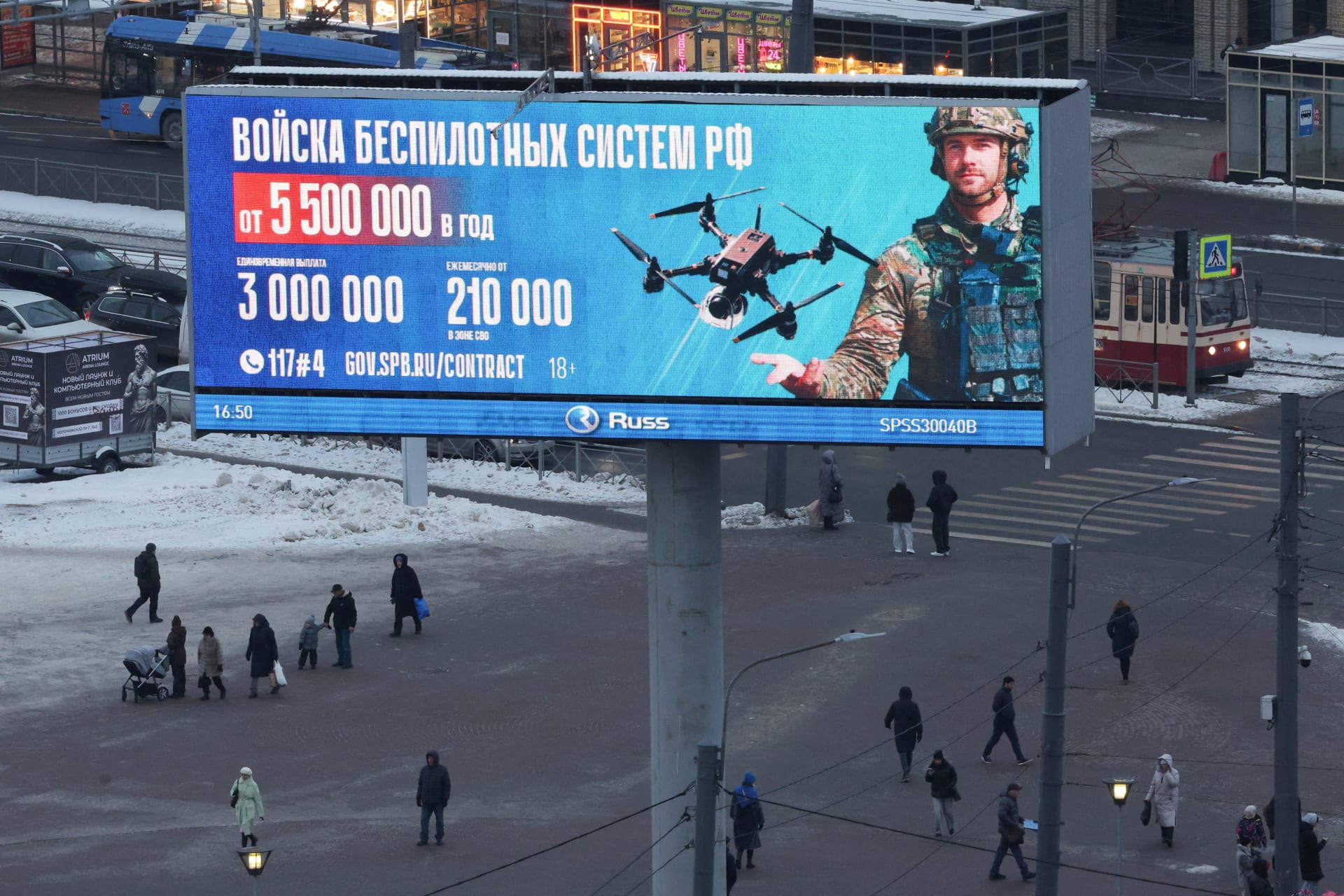 A large digital billboard advertising contract military service in Russia's Unmanned Systems Forces towers over pedestrians crossing a snowy square in St. Petersburg.