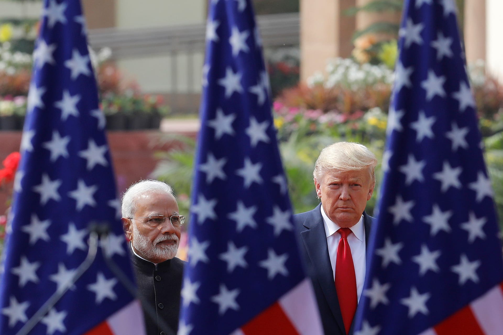 Narendra Modi and Donald Trump face the camera, separated and framed by three U.S. flags.