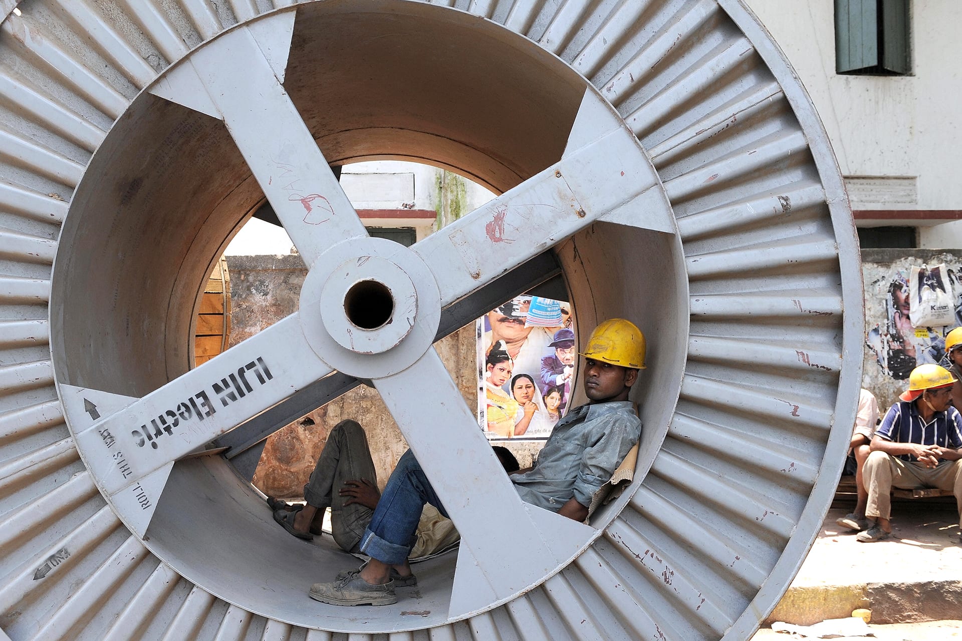 Two workers lay down inside the inner drum of a wheel of electrical wire.