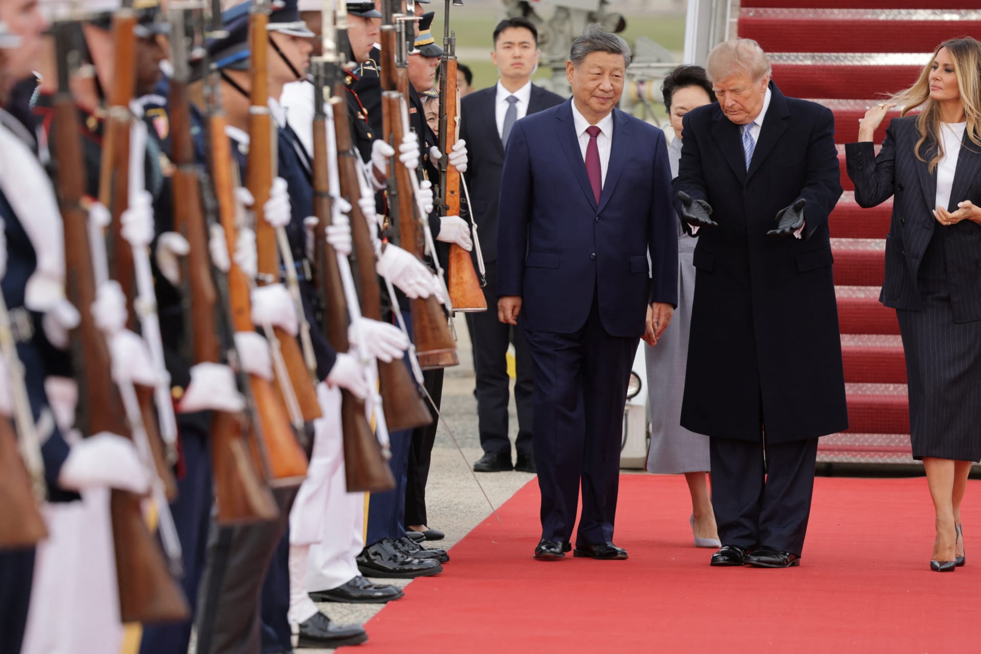 Xi Jinping and Donald Trump walk side by side down a red carpet past a military honor guard holding rifles, having just descended the aircraft stairs at Joint Base Andrews