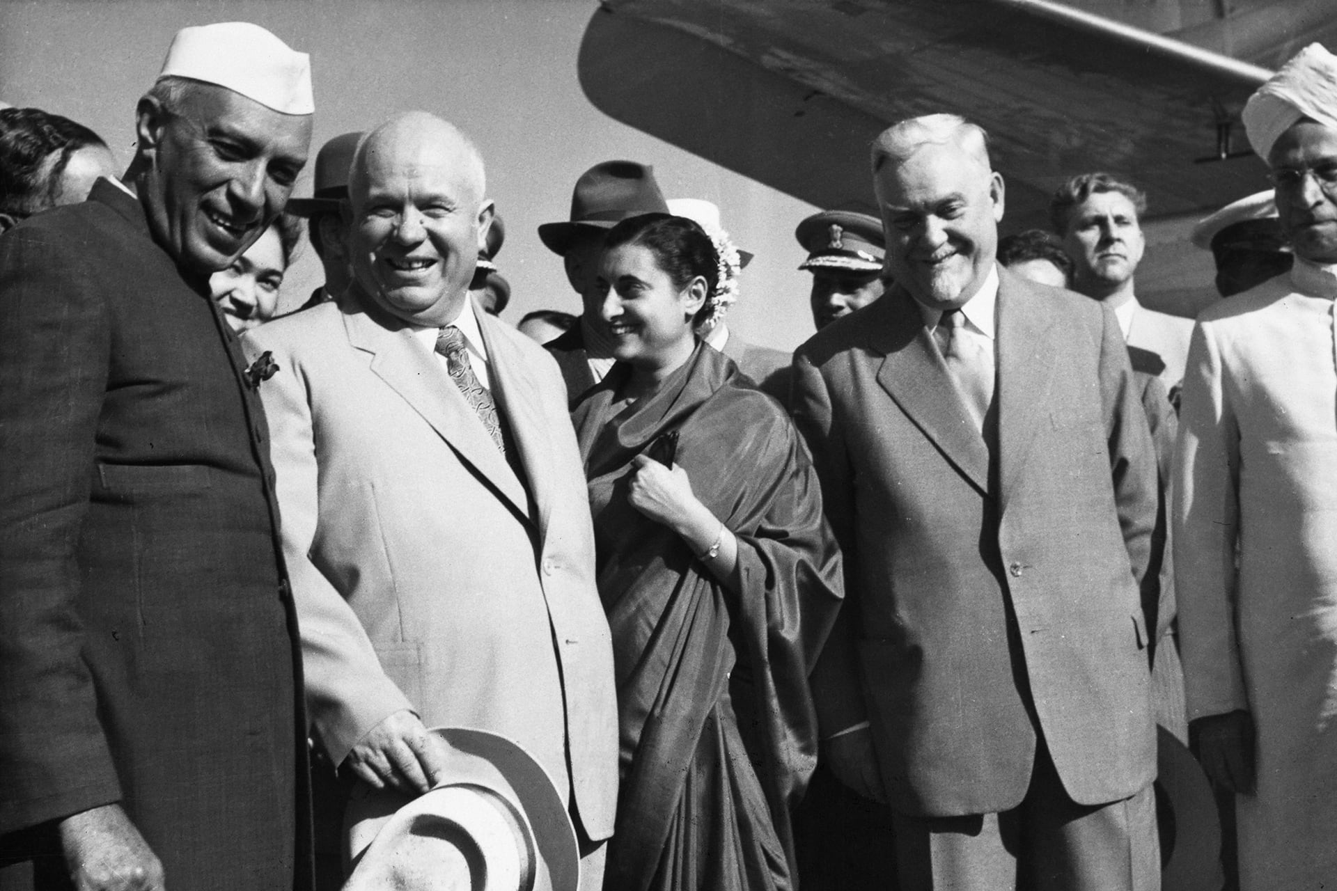Nehru, Krushchev, Gandhi, and Bulganin standing in a row, surrounded by aids, at the airport.