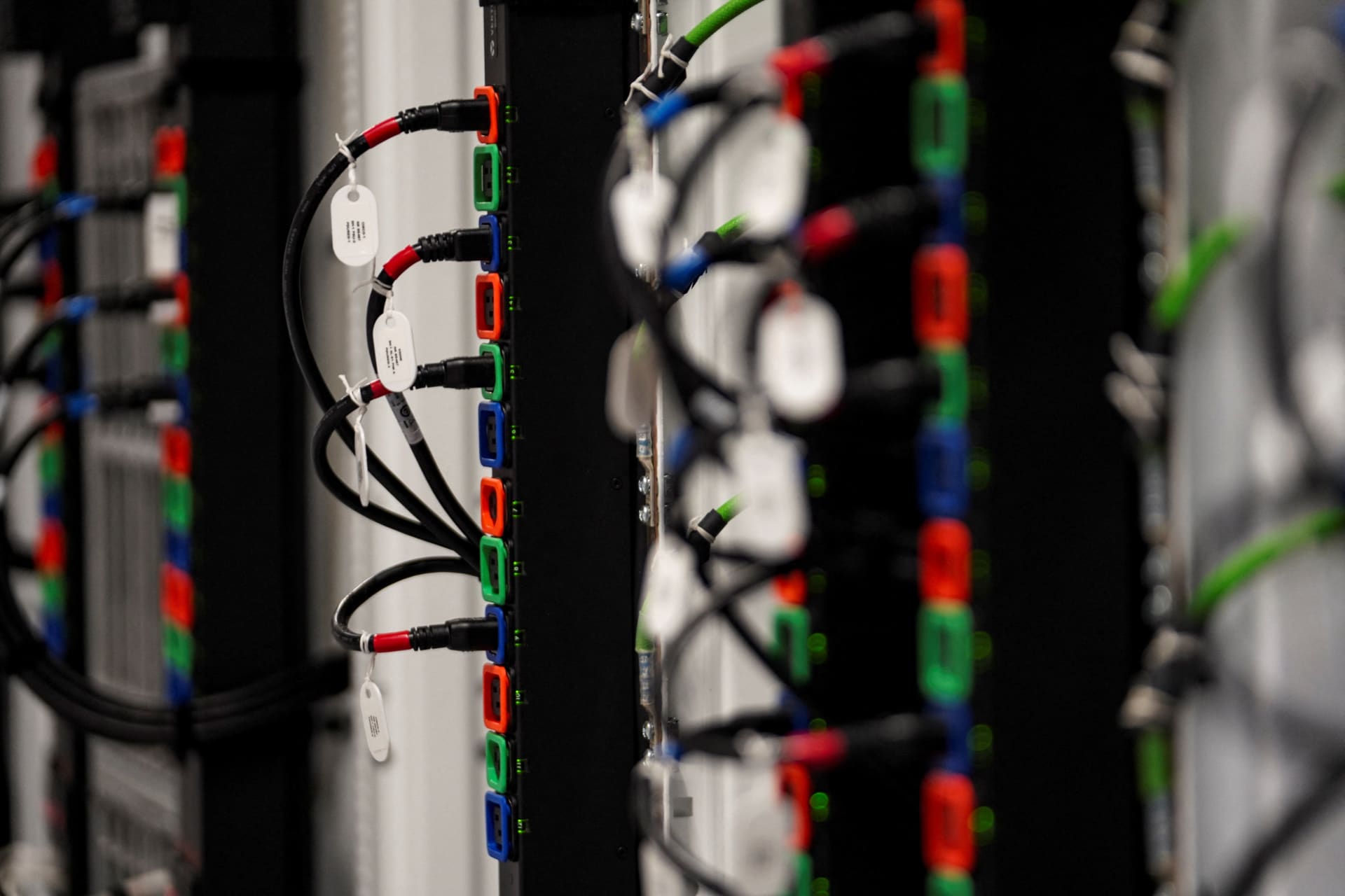 Close-up of black cables plugged into color-coded ports on a row of server racks inside a data center.