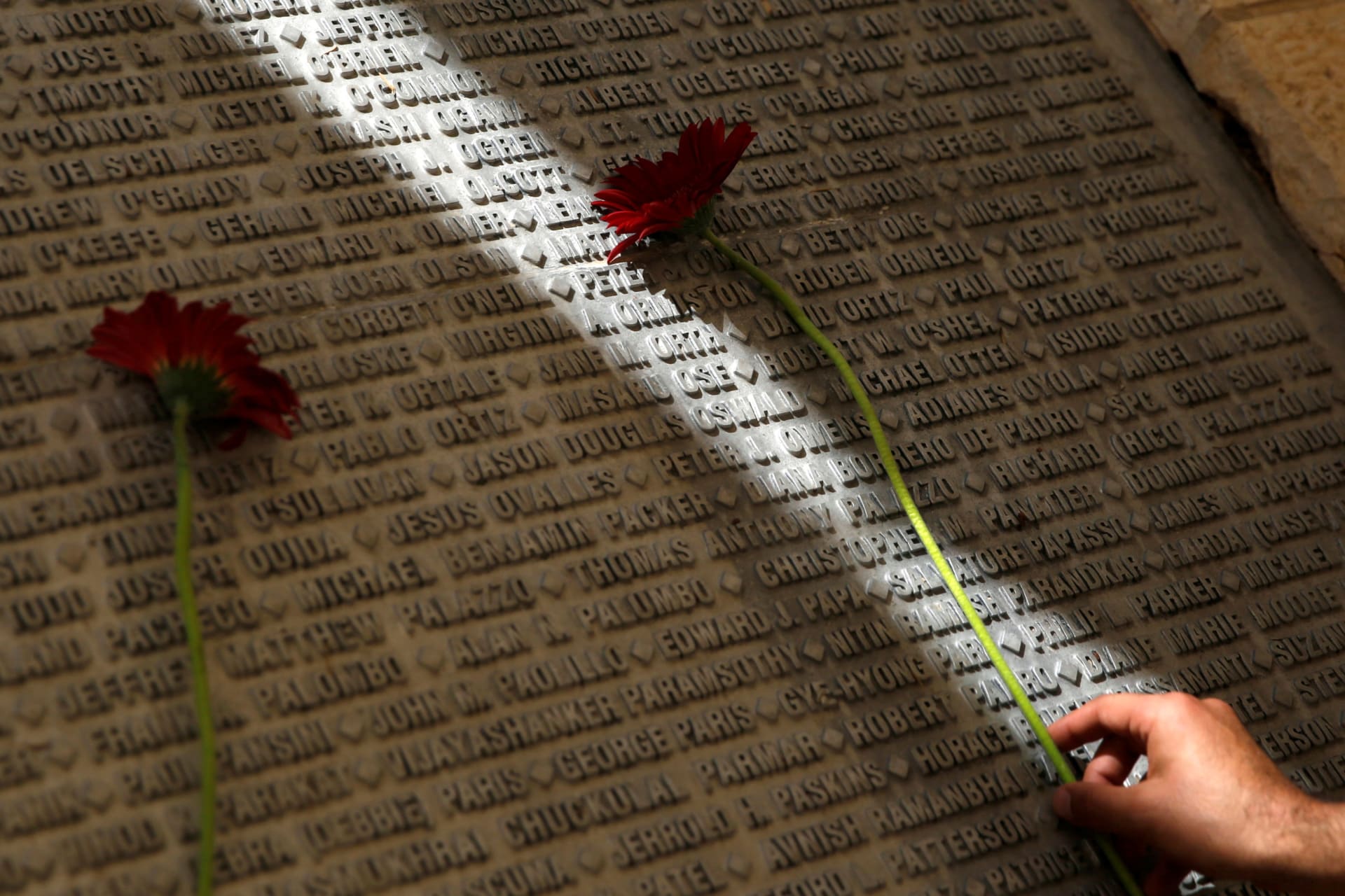 A man lays a flower on a monument engraved with names of victims of the September 11th attacks