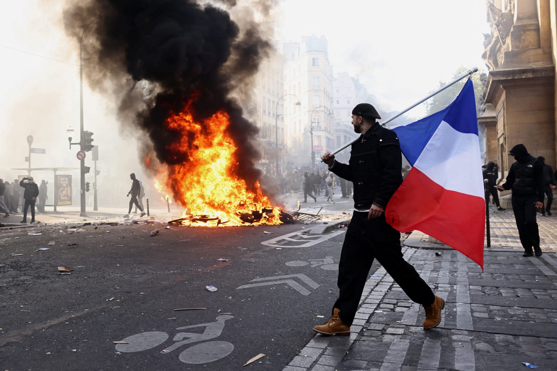 <p>A protester holds a French flag next to burning objects amid clashes in a street near the Place de Republique during a day of demonstrations in Paris, France, October 17, 2026. </p>
