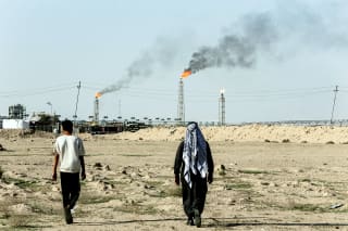 People walk near farmland by the Zubair oil field as gas flares rise in the distance, in Zubair Mishrif, Basra, Iraq, amid regional tensions following the recent disruption to shipping in the Strait of Hormuz and the U.S.-Israeli conflict with Iran on March 9, 2026.