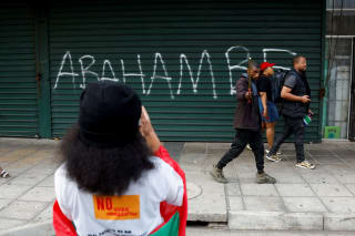 <p>People walk past a slogan reading, “They must go,” written on the shutter of a shop as anti-immigrant protesters march on the day of an unofficial deadline set by anti-immigrant groups for all undocumented migrants to leave, in Durban, South Africa, on June 30, 2026. </p>
