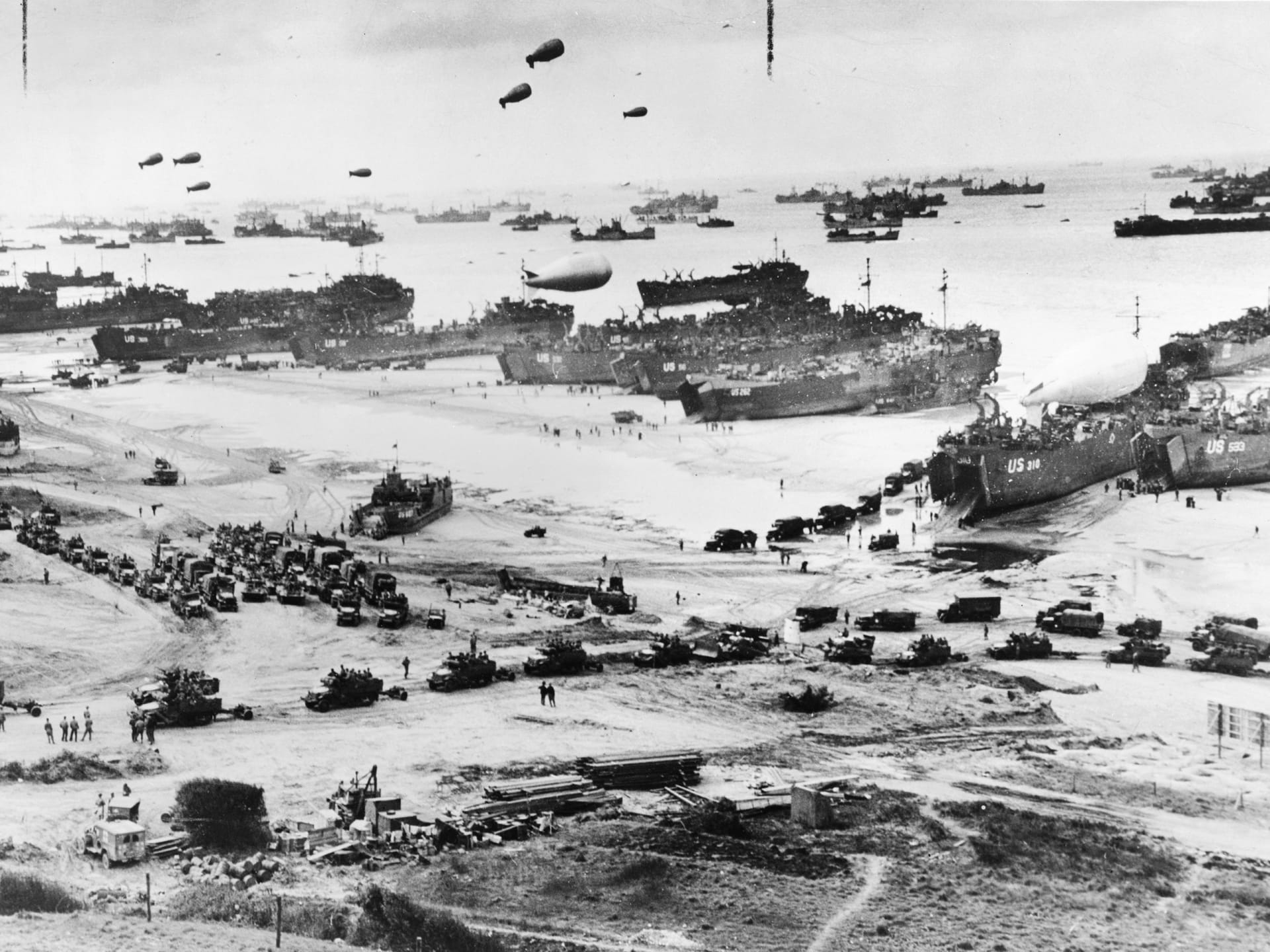 Bird's-eye view of landing craft, barrage balloons, and allied troops landing in Normandy, France on D-Day.