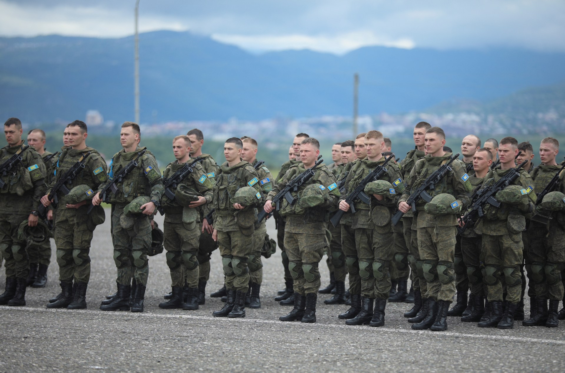 Soldiers stand at attention in front of mountains.