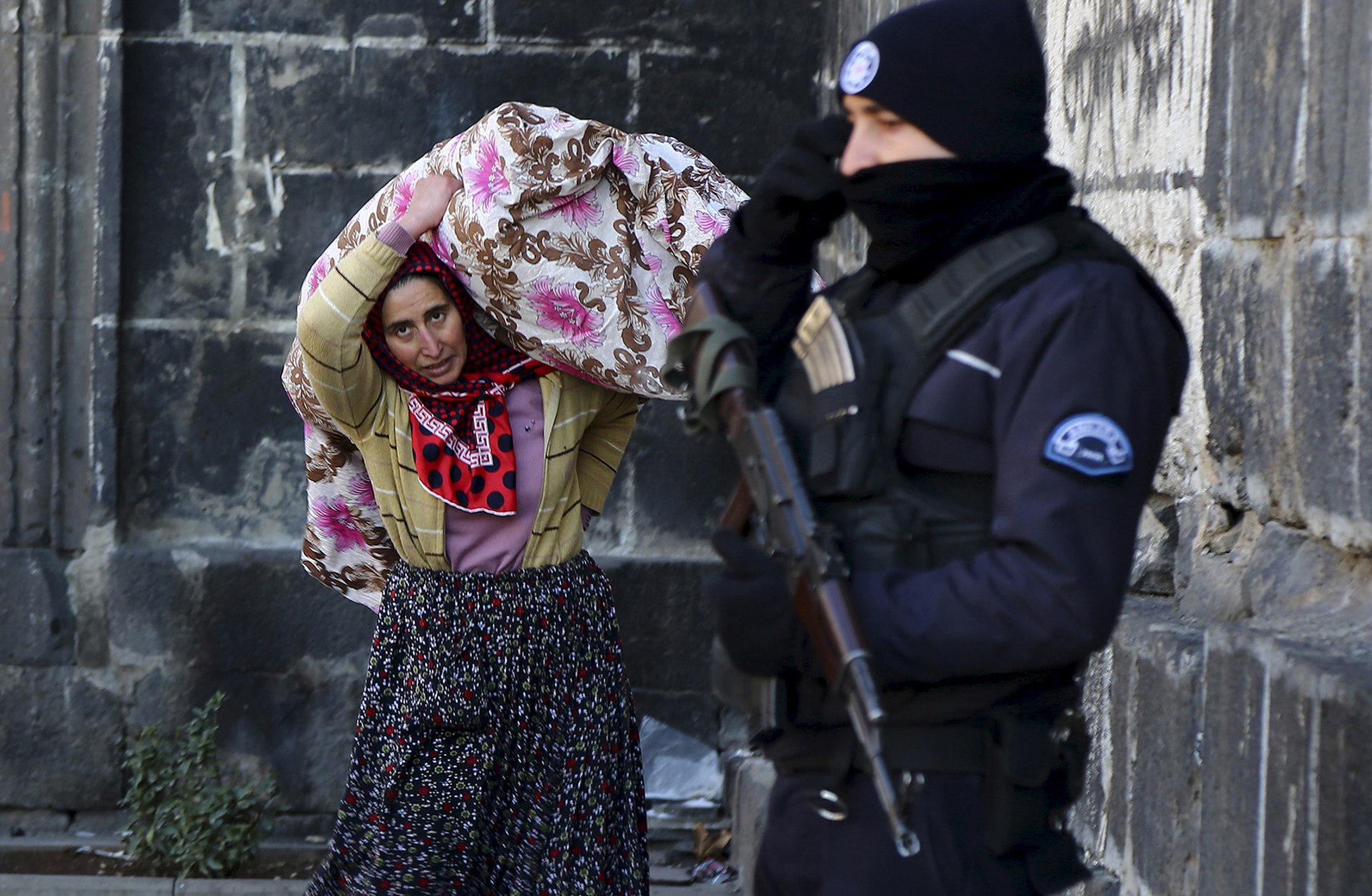 A resident carries her belongings past a police officer as she flees from Sur district, which is partially under curfew, in the Kurdish-dominated southeastern city of Diyarbakir, Turkey on January 27, 2016.
