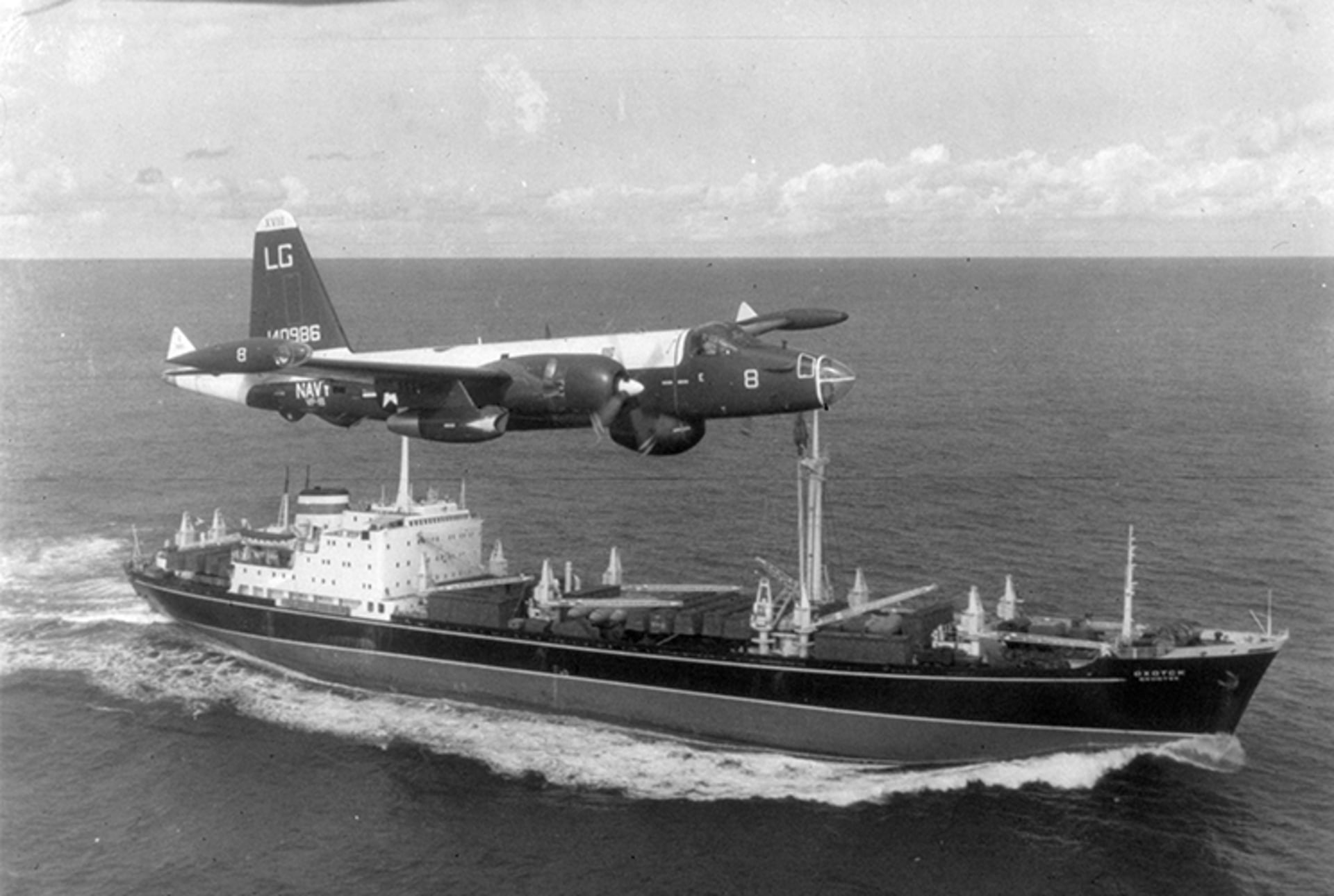 A black and white photo of a U.S. plane flying very closely over a Soviet freighter in the ocean.
