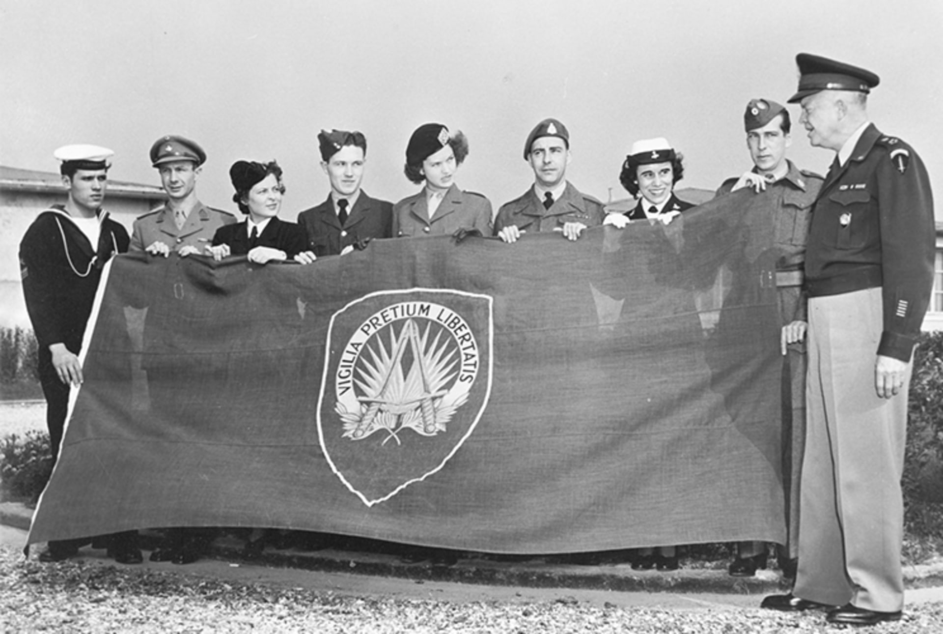 A black and white photo of General Dwight D. Eisenhower and members of the UN holding the first NATO flag. 