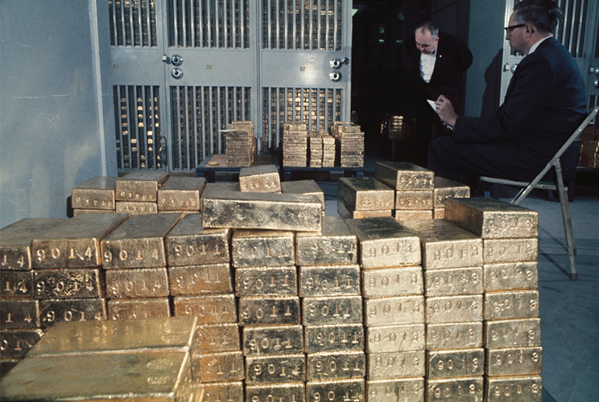 A photo of two men counting lots of gold bars in a basement. 