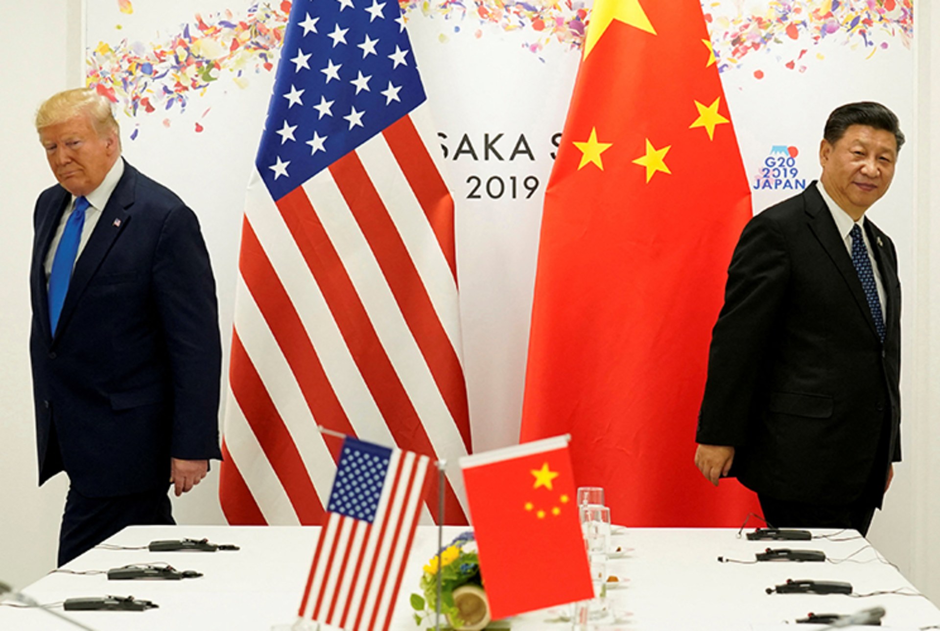 A photo of President Donald Trump and China's President Xi Jinping walking in opposite directions around a table as the U.S. and Chinese flags are behind them.
