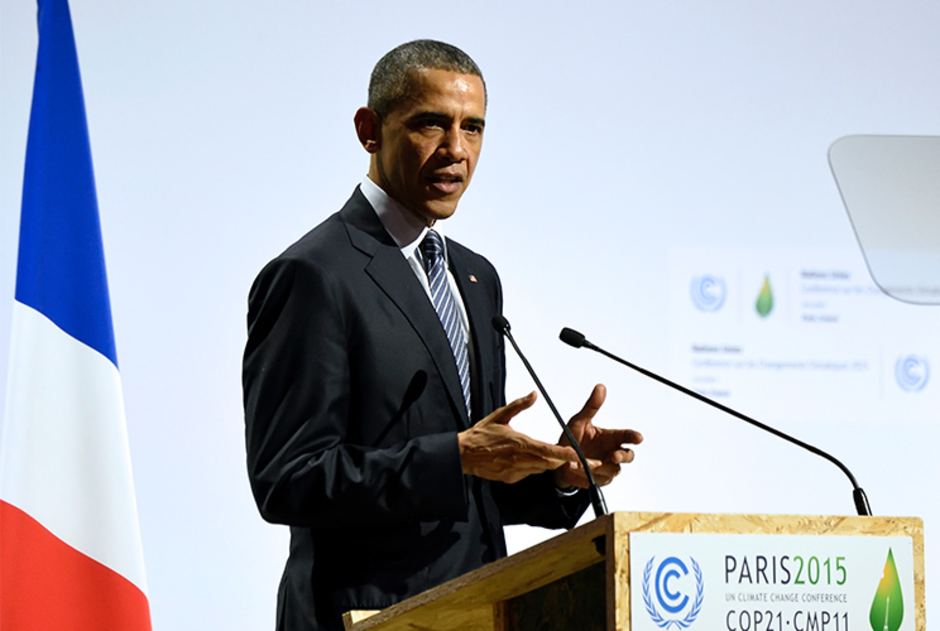 A photo of President Barack Obama speaking at a podium at the COP 21 UN conference while a French flag stands behind him.