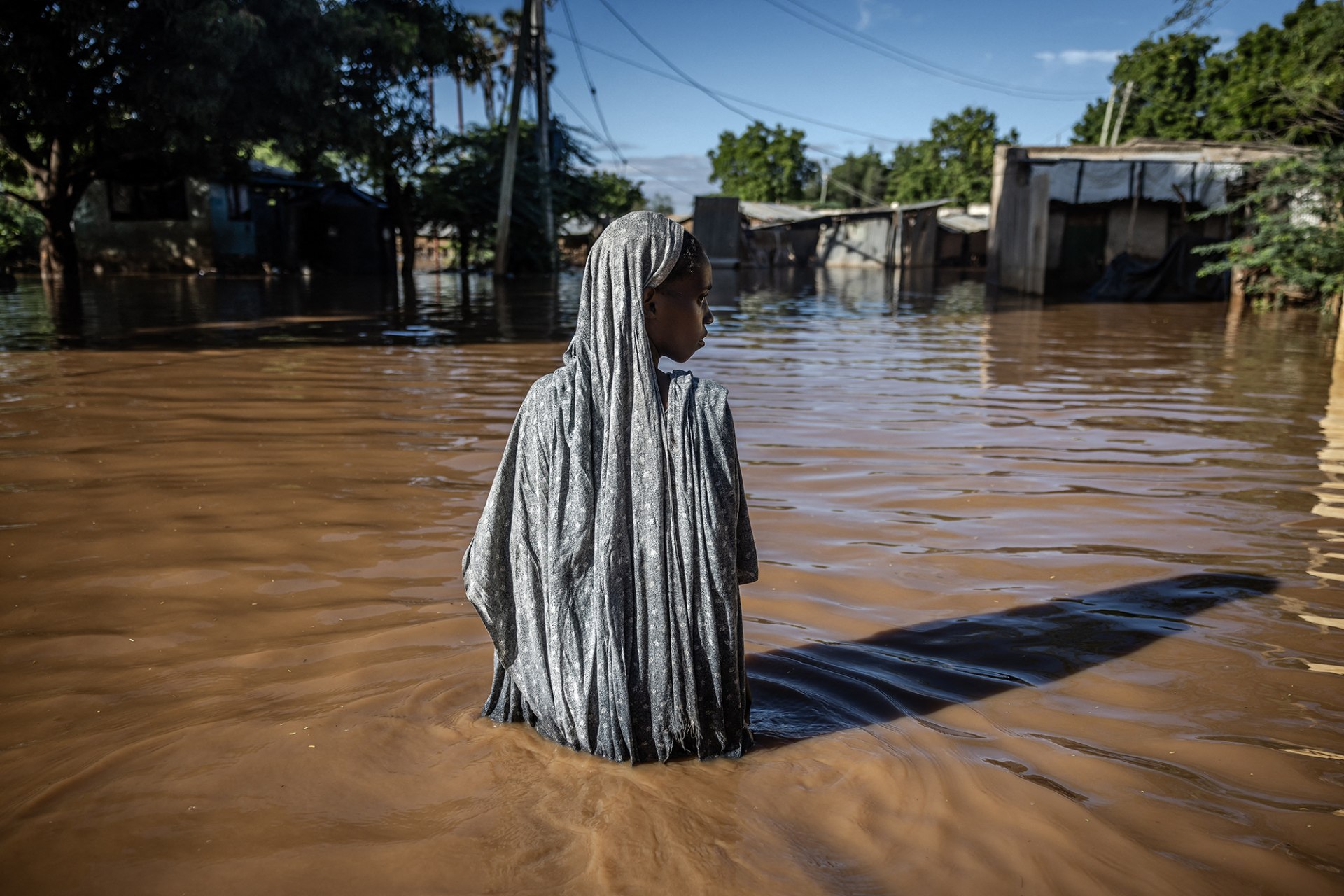 A woman wades through flood water up to her hips in Kenya.