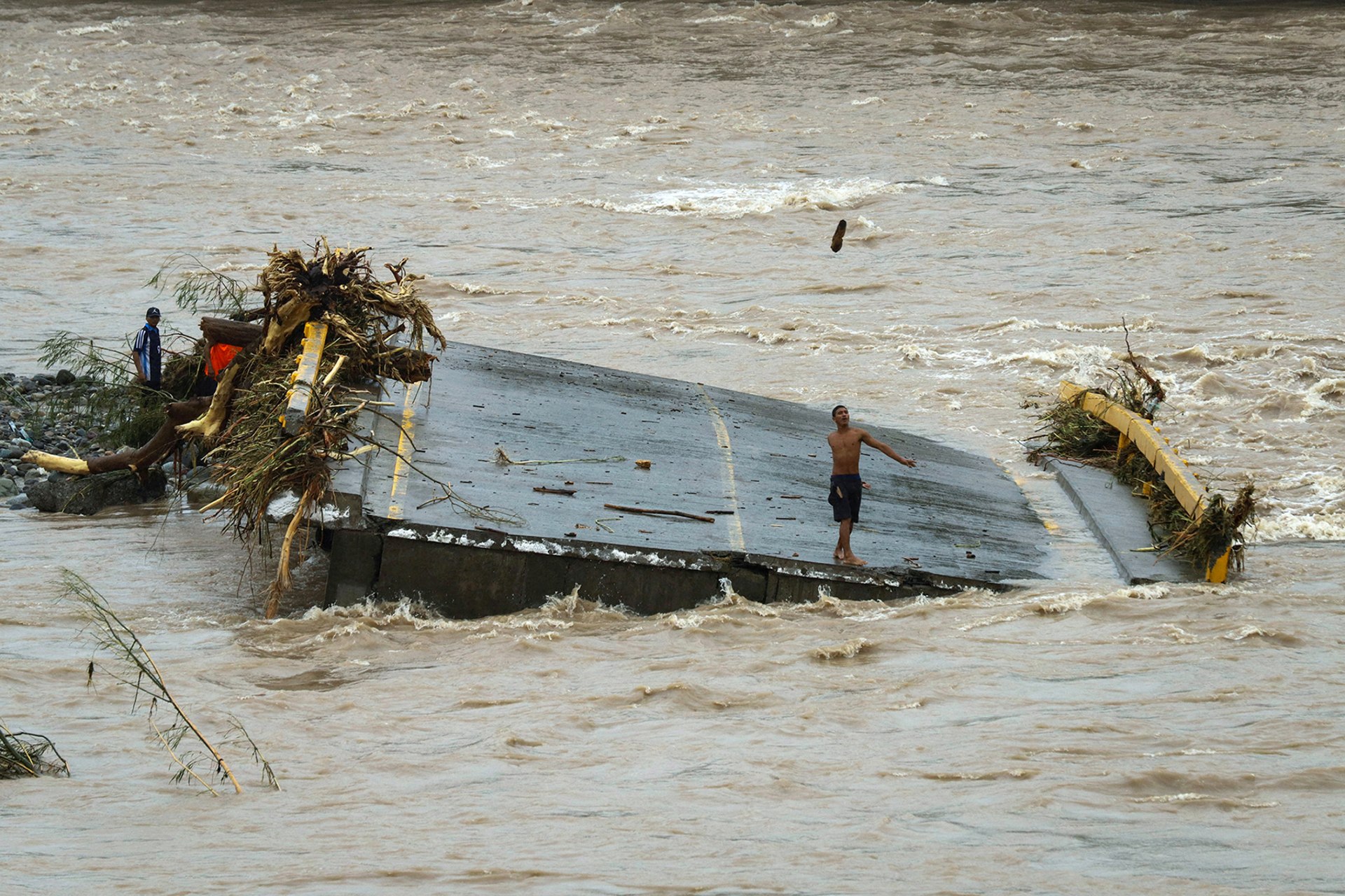 A man throws an object while standing on a section of a bridge destroyed during the aftermath of a tropical storm in Honduras.