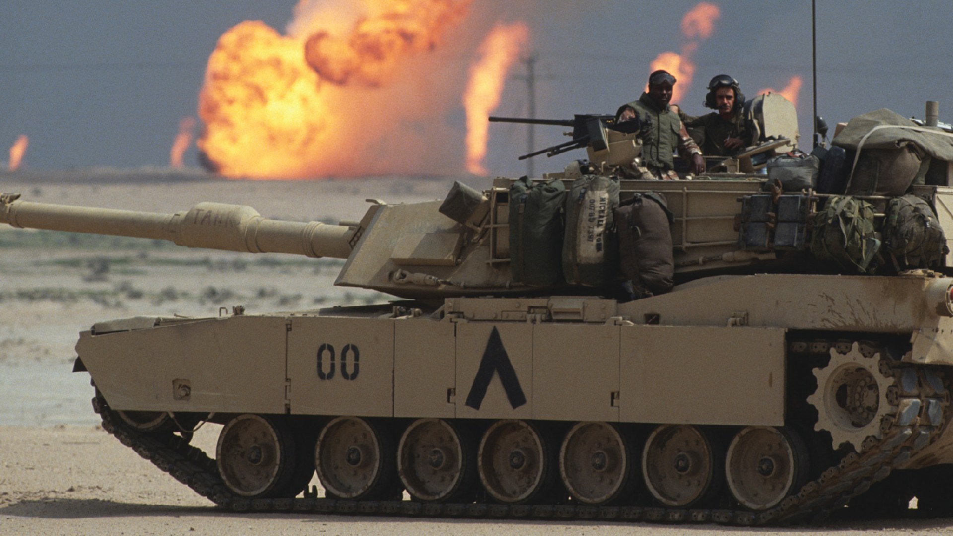 American soldiers stand in the turret of a tank in Kuwait as oil wells burn near the Iraqi border.
