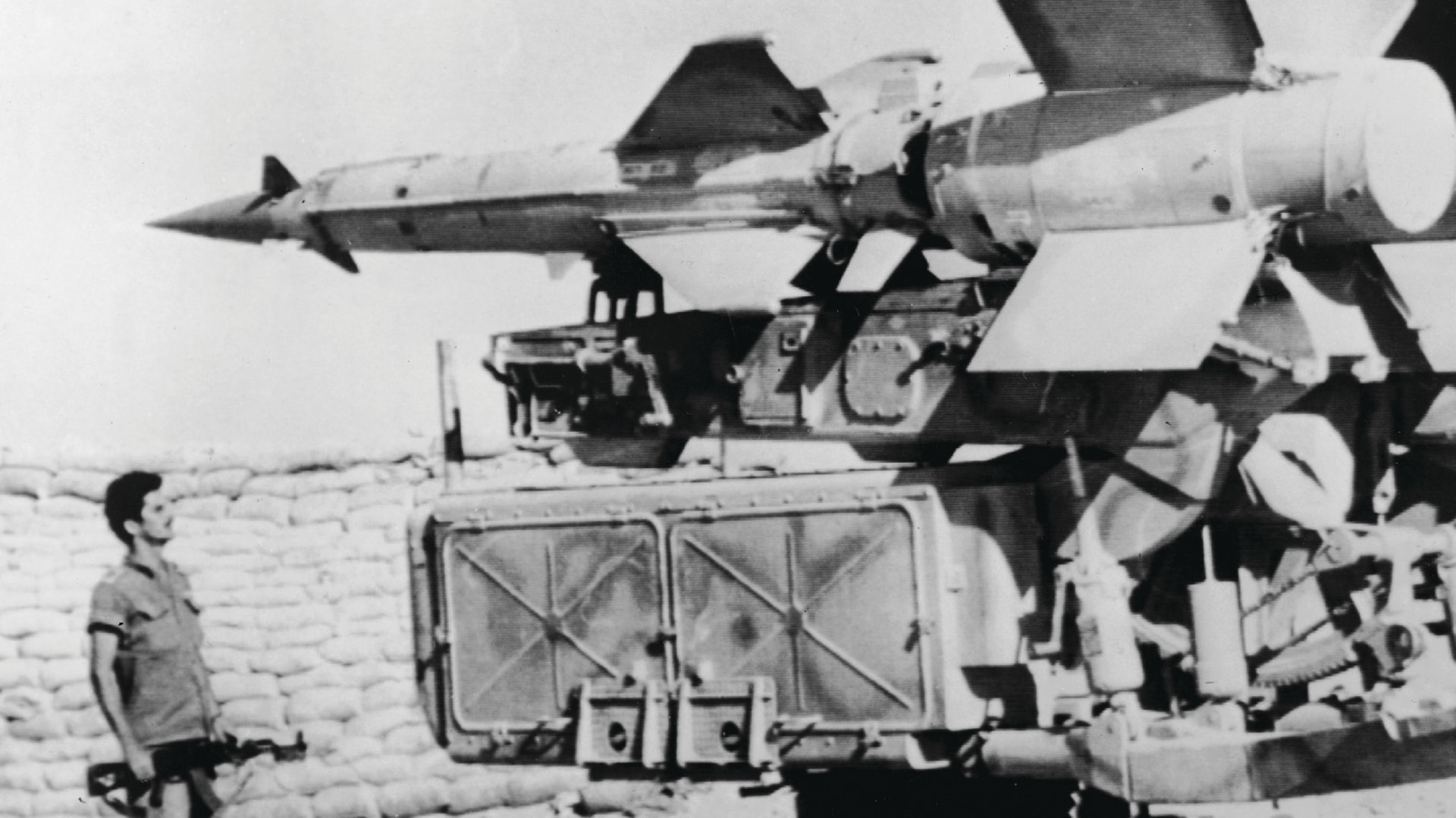 A black and white photo shows Israeli soldier looking at a Soviet-built Egyptian missile launcher captured by Israeli forces on the bank of the Suez Canal.