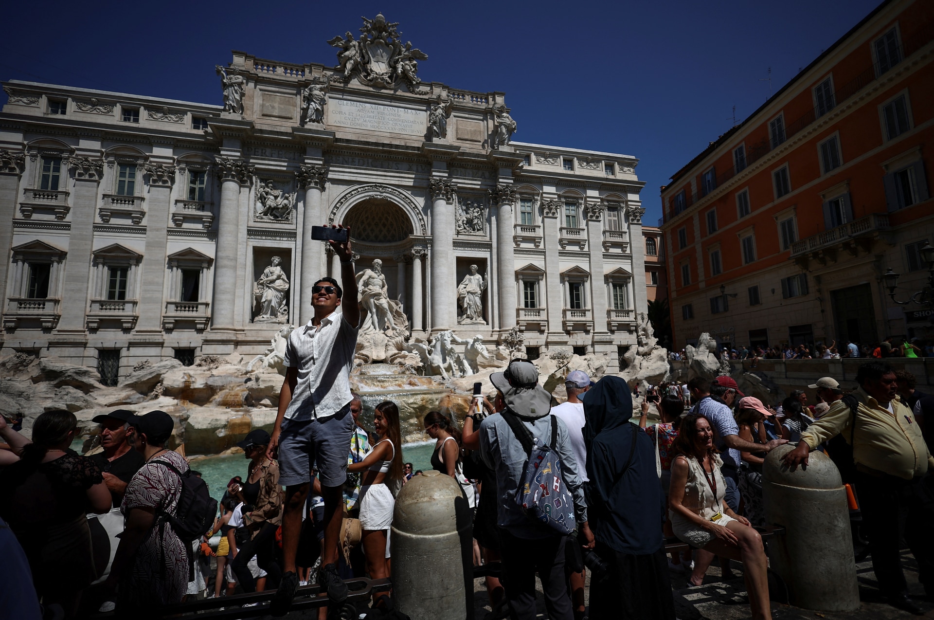 Crowds of tourists visit the Trevi Fountain in Rome, Italy and take photos.