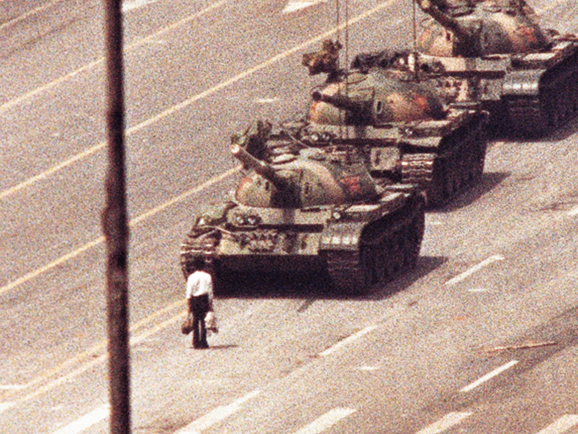 A grainy image shows a man standing in front of a convoy of tanks in the Avenue of Eternal Peace in Tiananmen Square in Beijing, China.