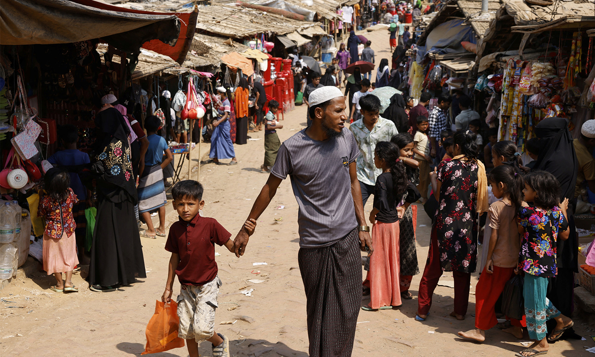A Rohingya refugee man walks and holds a child's hand in a market, at the Rohingya refugee camp in Cox's Bazar, Bangladesh.