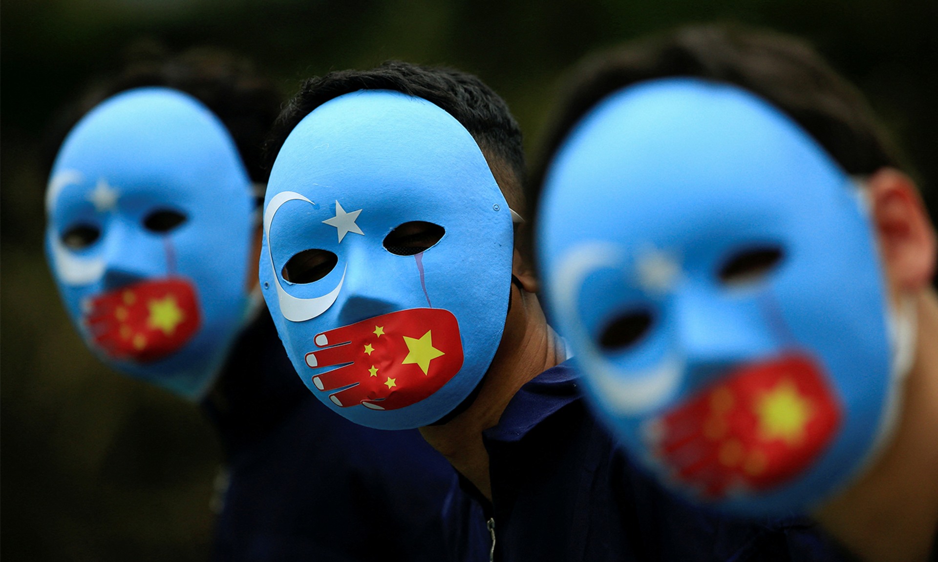 Activists wearing blue masks showing the flag of East Turkestan covered by a hand showing the Chinese flag, protest against China's treatment towards the ethnic Uyghurs.