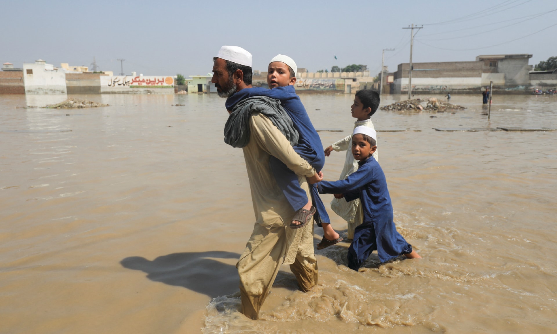 A man walks with children through flood water along a road, during the monsoon season in Nowshera, Pakistan August 30, 2022.