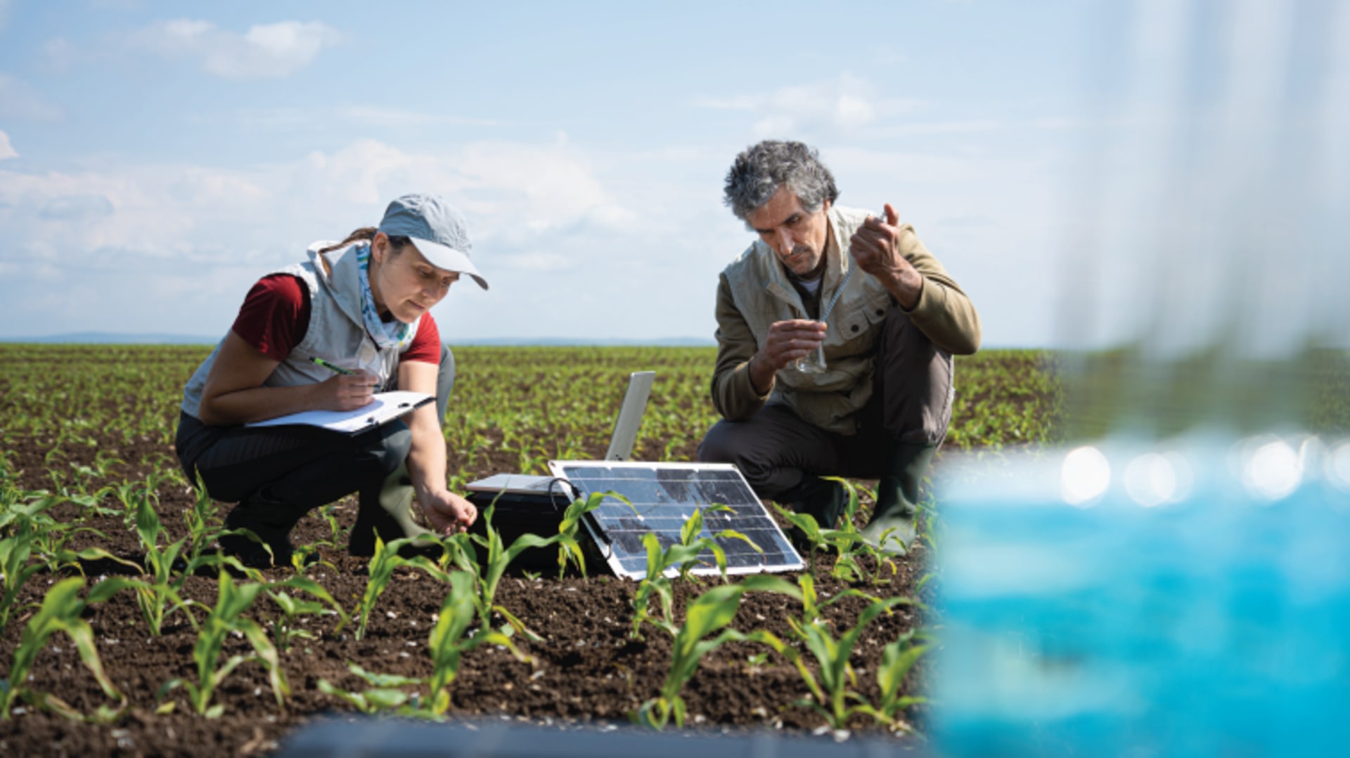 Agronomists crouch in a field and survey soil using mobile lab and AI-driven technologies.