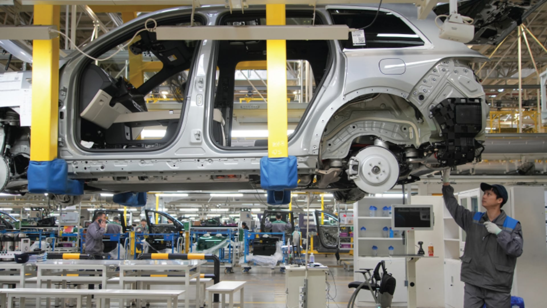 An autoworker reaches up to assemble a car on a car lift at a major Chinese EV maker.