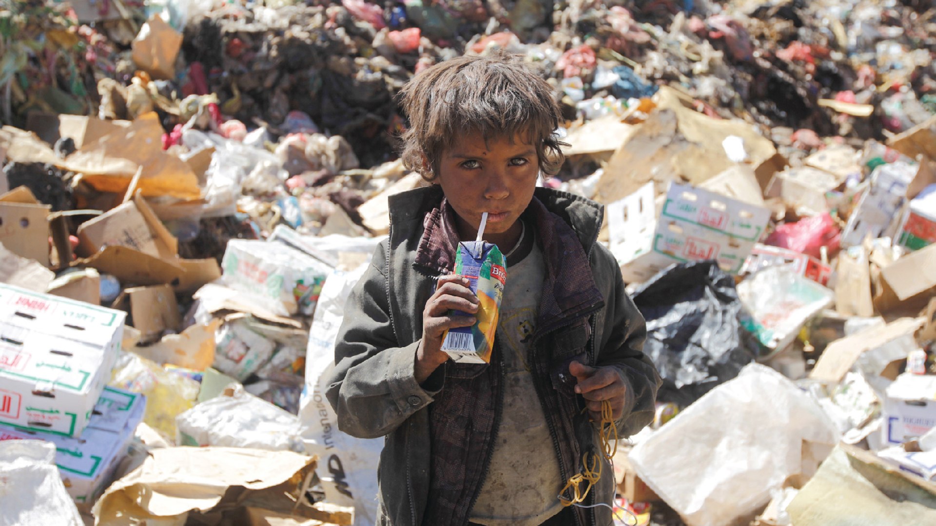 A Yemeni boy looks at the camera and drinks expired juice at a landfill on the outskirts of Sanaa, Yemen.