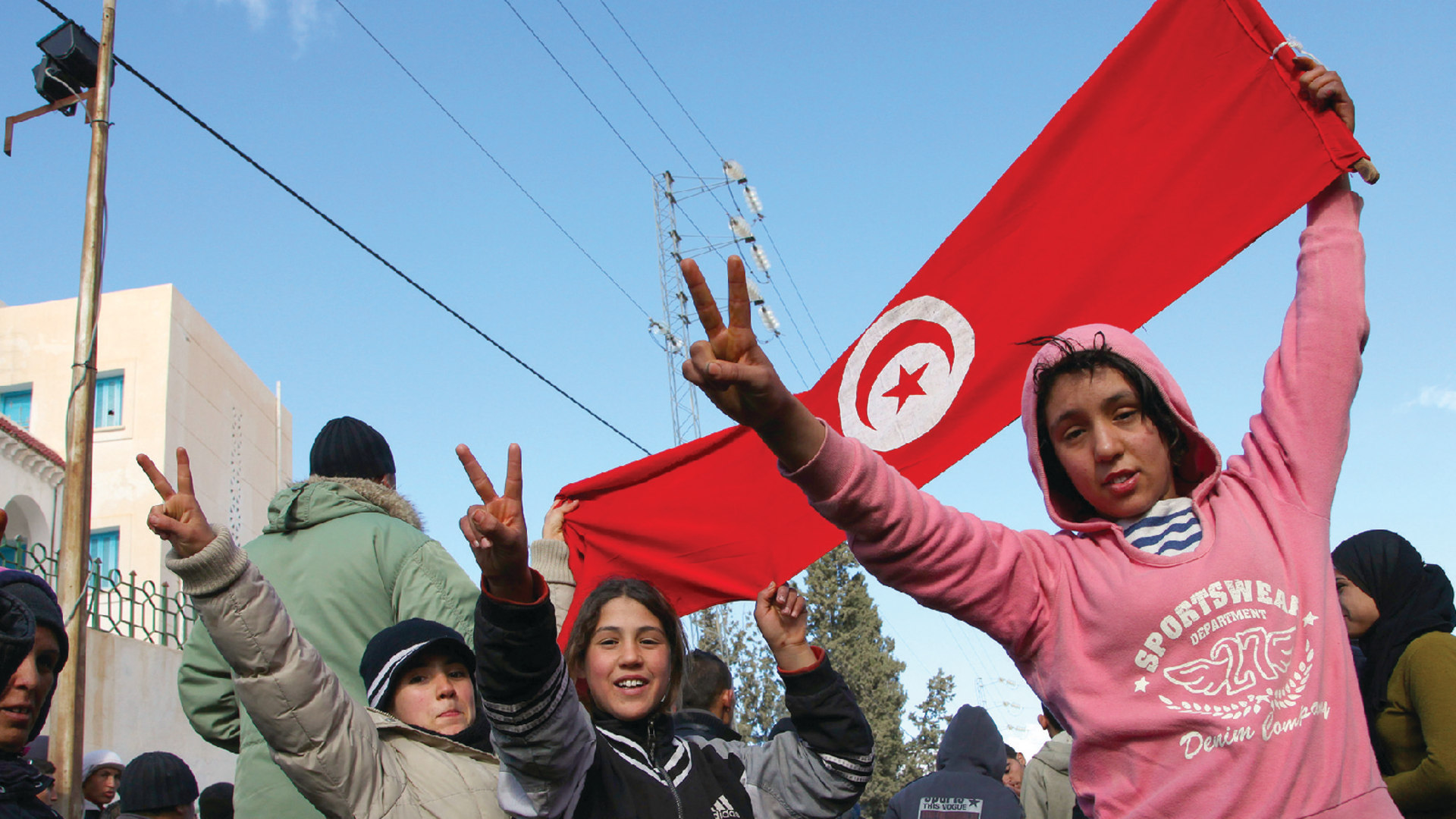 Three kids hold up a Tunisian flag and peace signs as people demonstrate against Tunisia's Ben Ali Regime in Kasserine, Tunisia.
